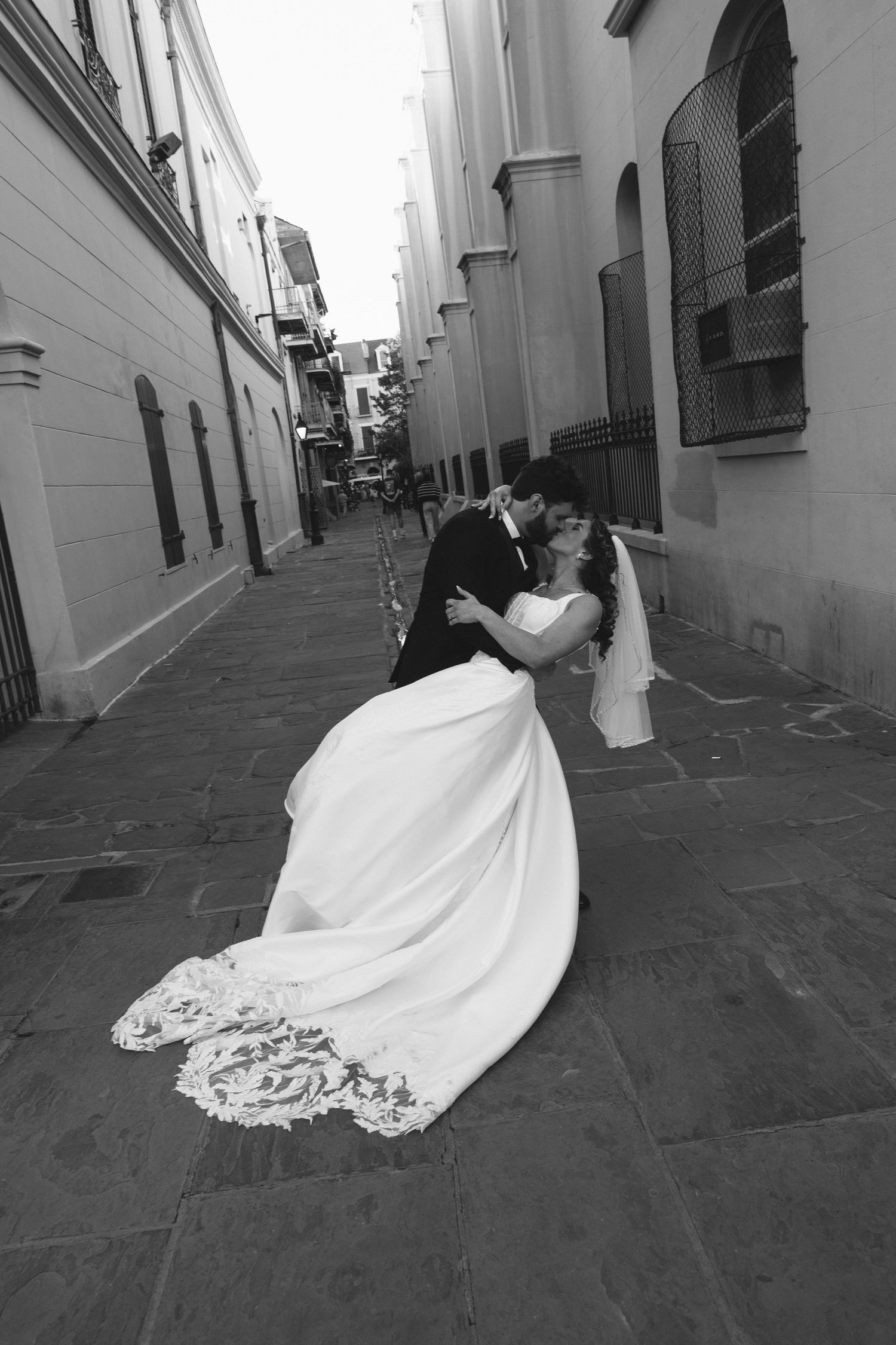 Black and white photo of a bride and groom sharing a romantic dip kiss on a cobblestone alley.