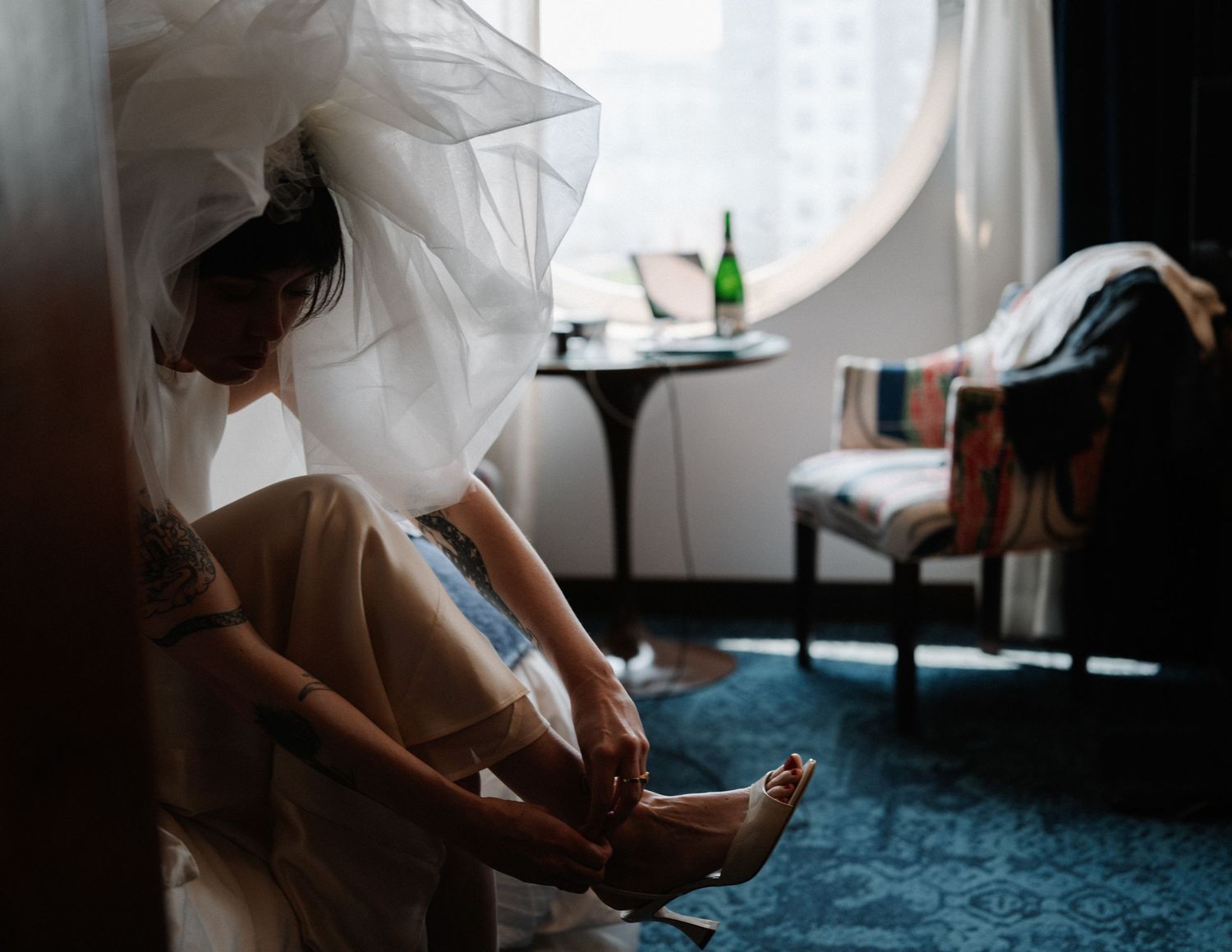 Getting ready scene showing white wedding dress and veil details in a sunlit room.