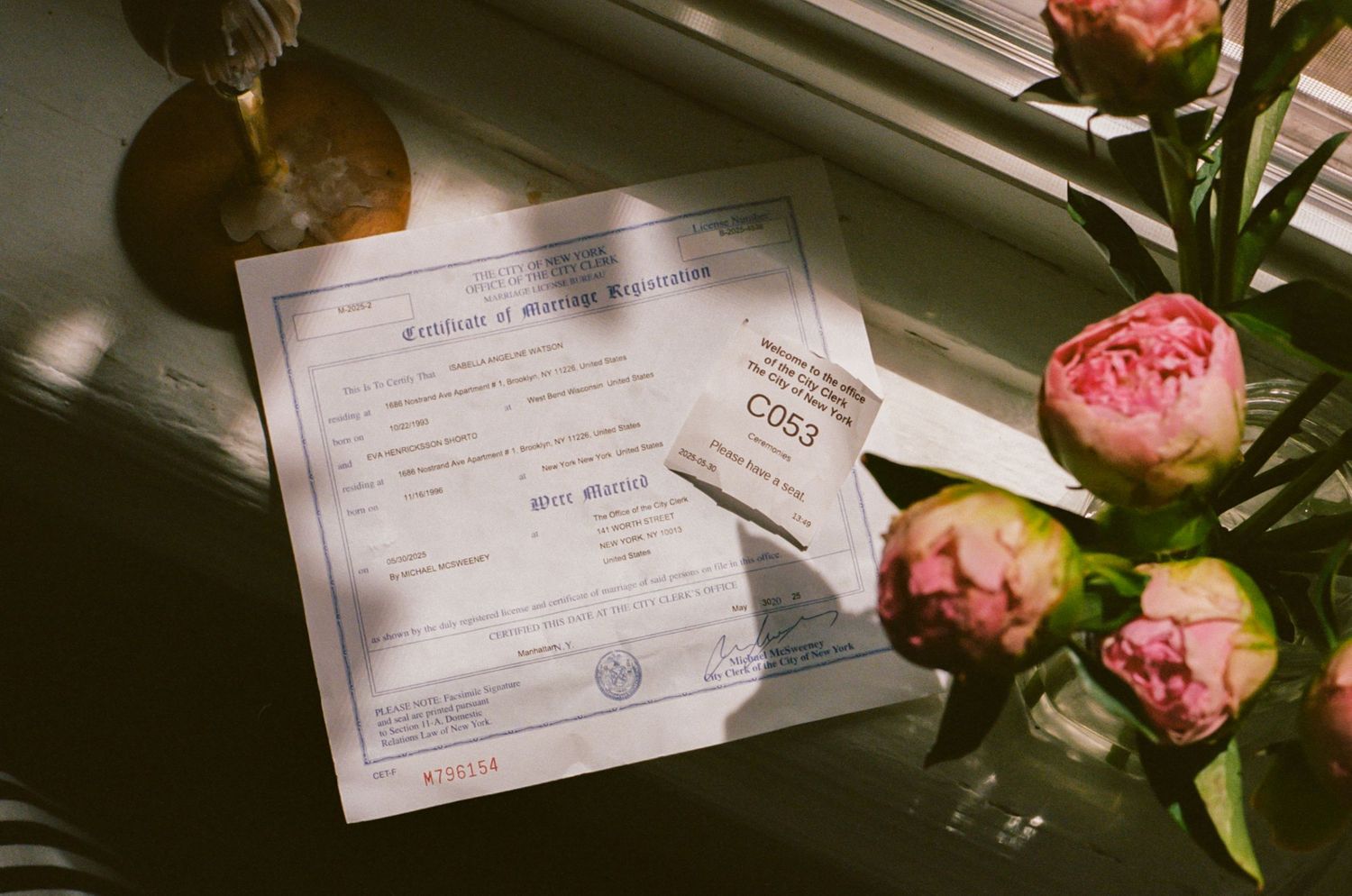 Marriage certificate document with pink peonies in soft window light.