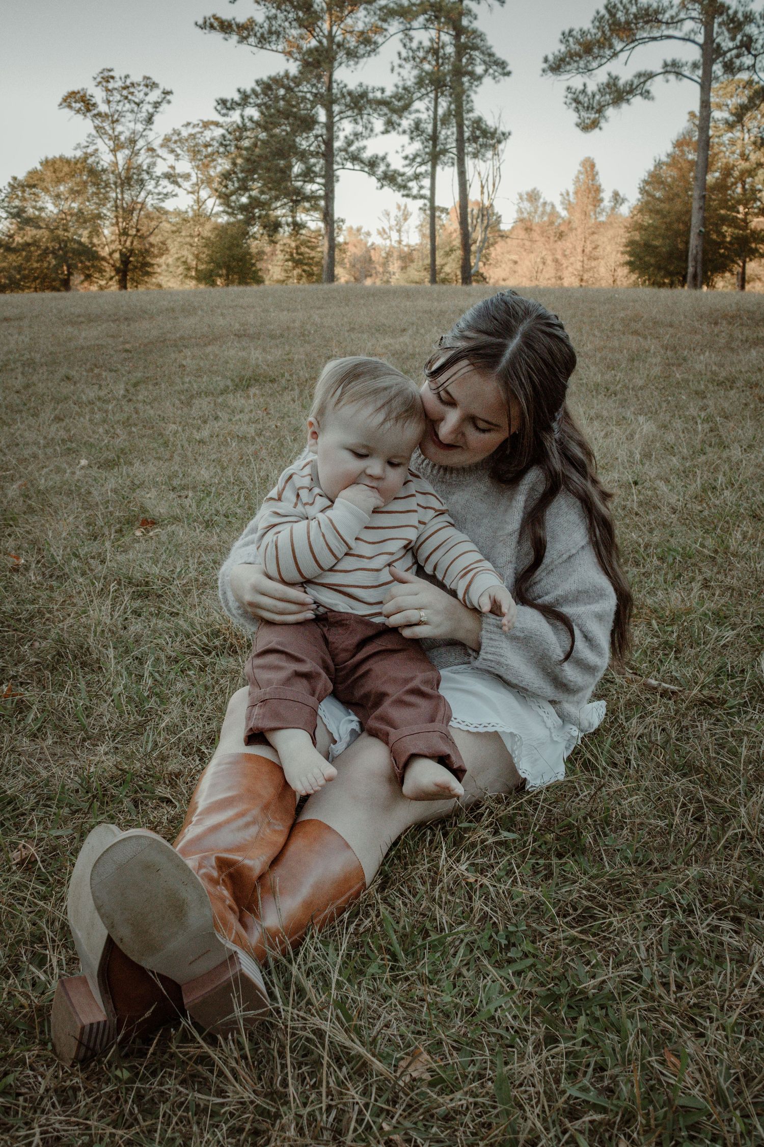 A sweet moment captured in nature as two people share laughter while sitting together on grassy ground at sunset.