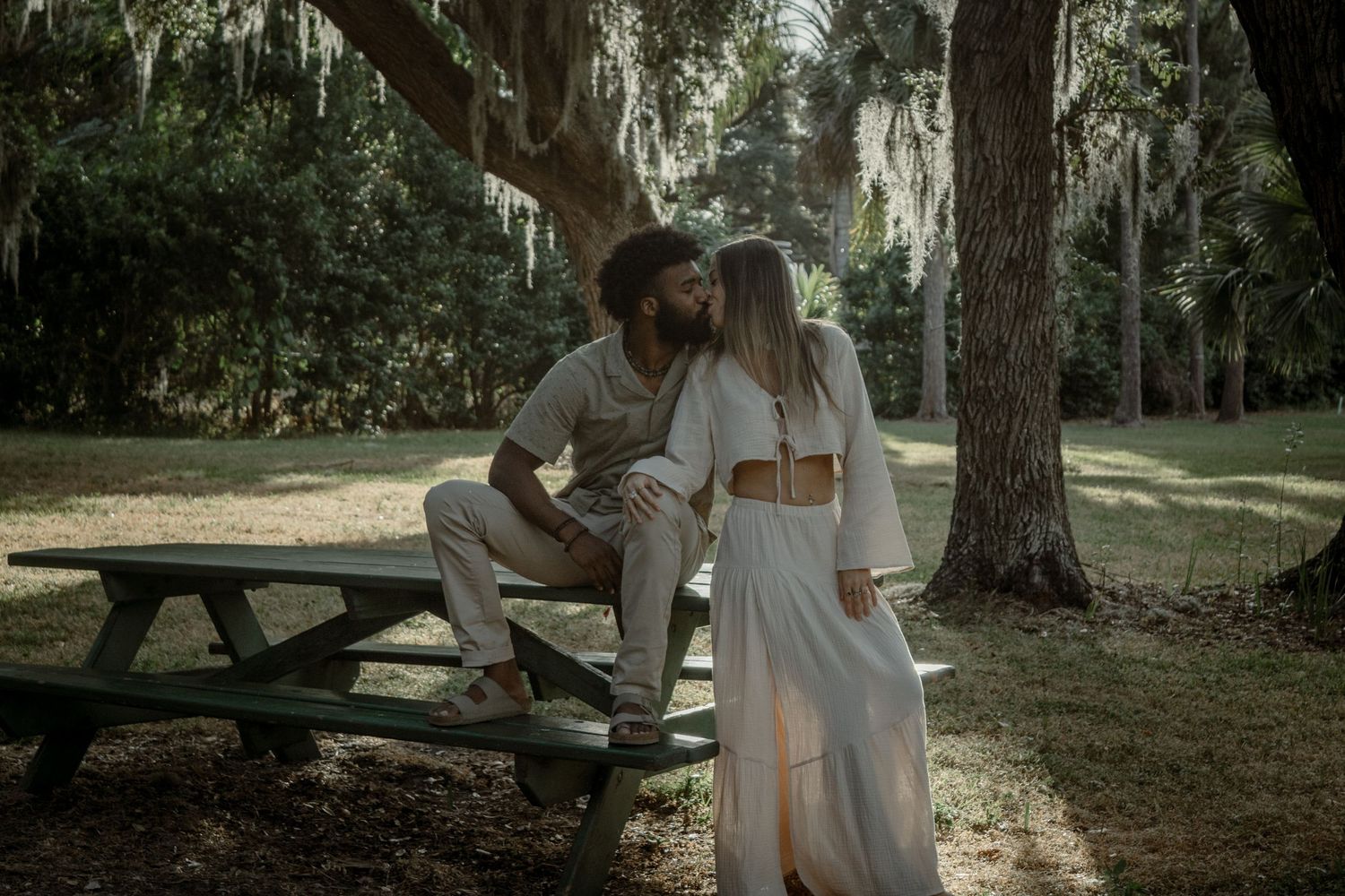 A romantic outdoor photo session under moss-draped trees in a sunlit park setting.