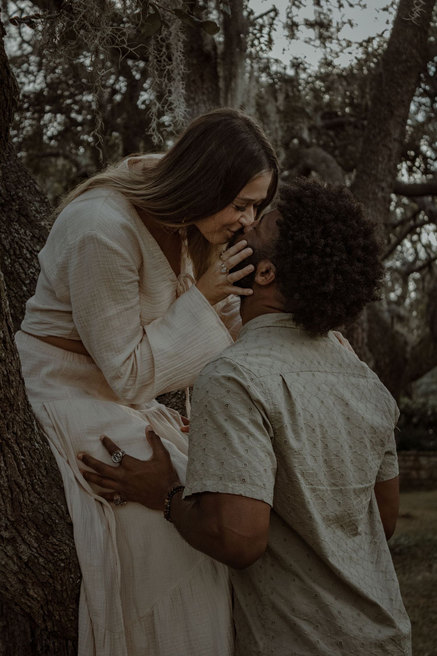 A tender embrace between a couple against a tree in a moody, atmospheric setting.