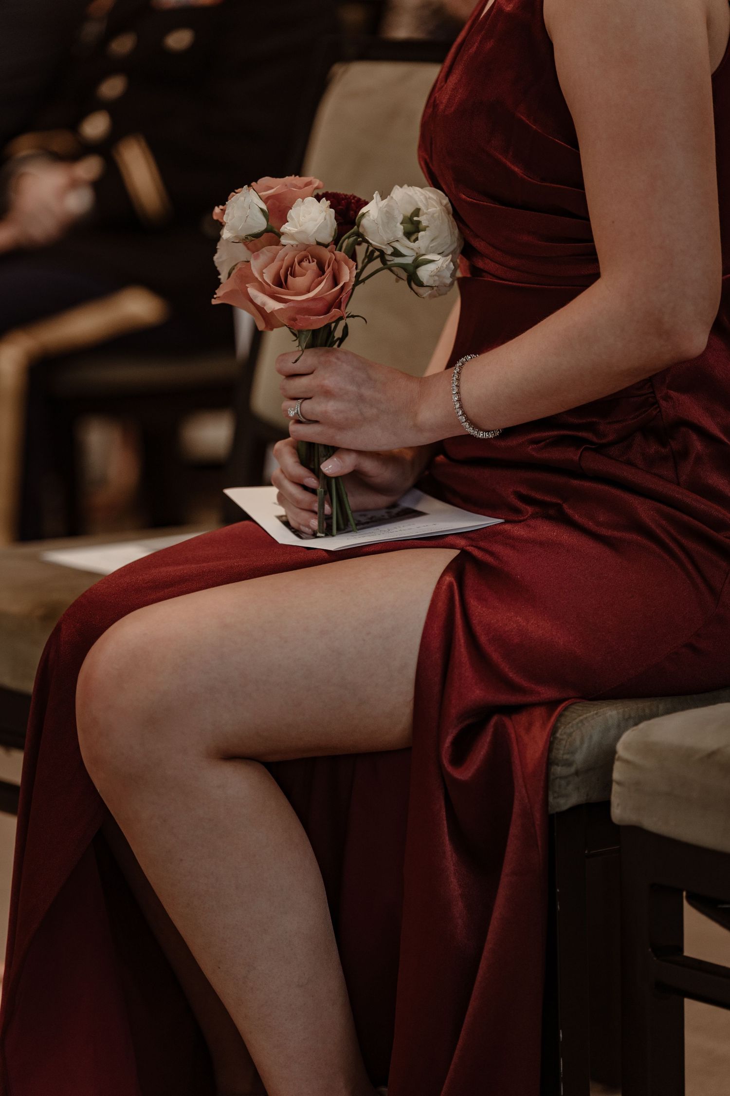 Bridesmaids in burgundy dresses hold pink roses while seated.