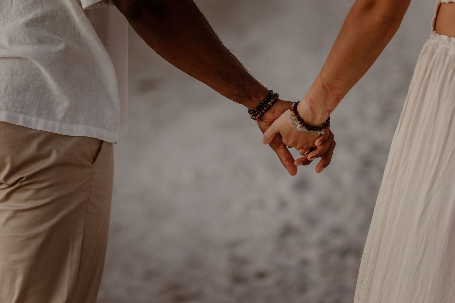 Couple walking hand in hand along a beach at sunset in casual attire.