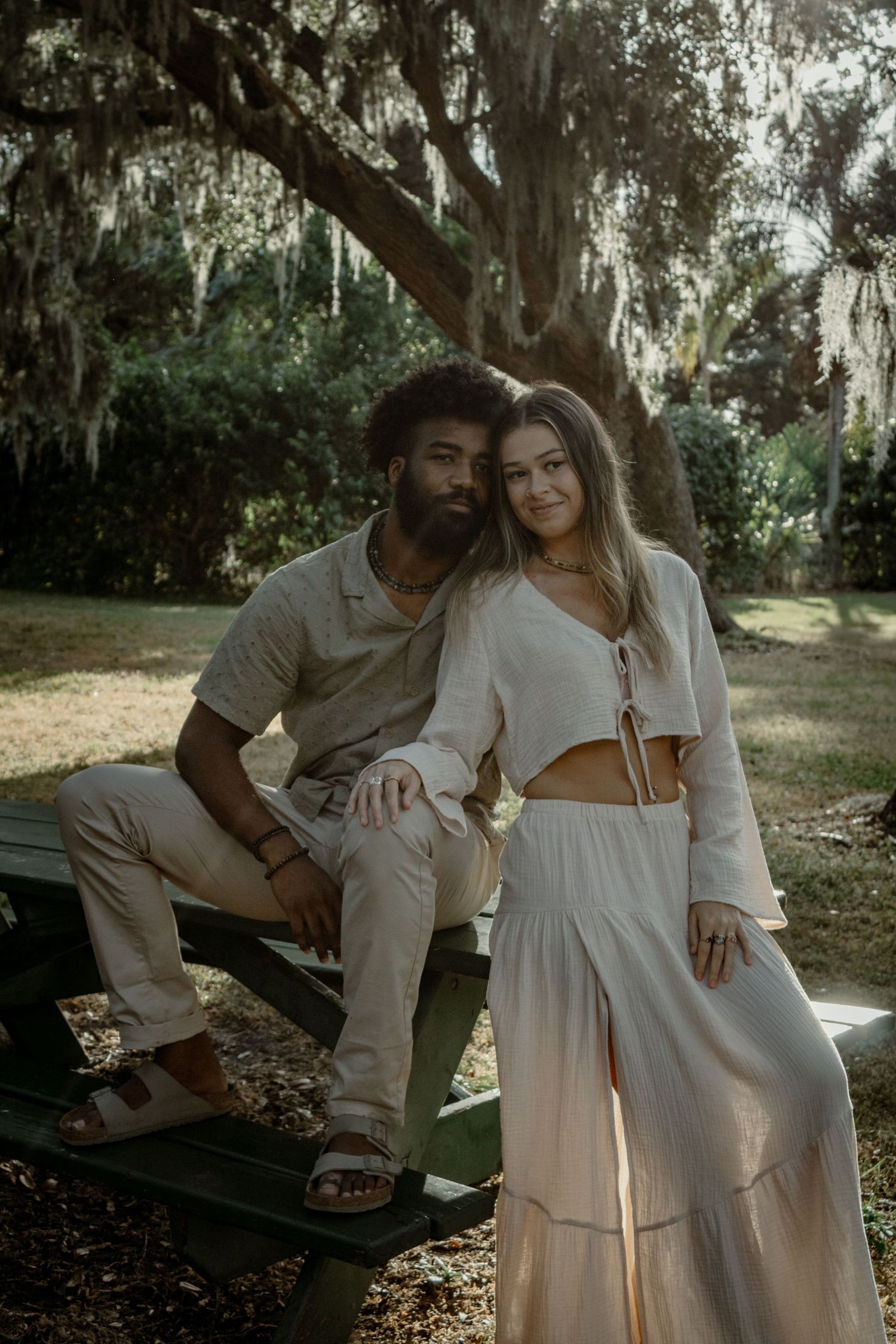 Romantic couple shares tender moments together on a park bench under moss-draped trees.