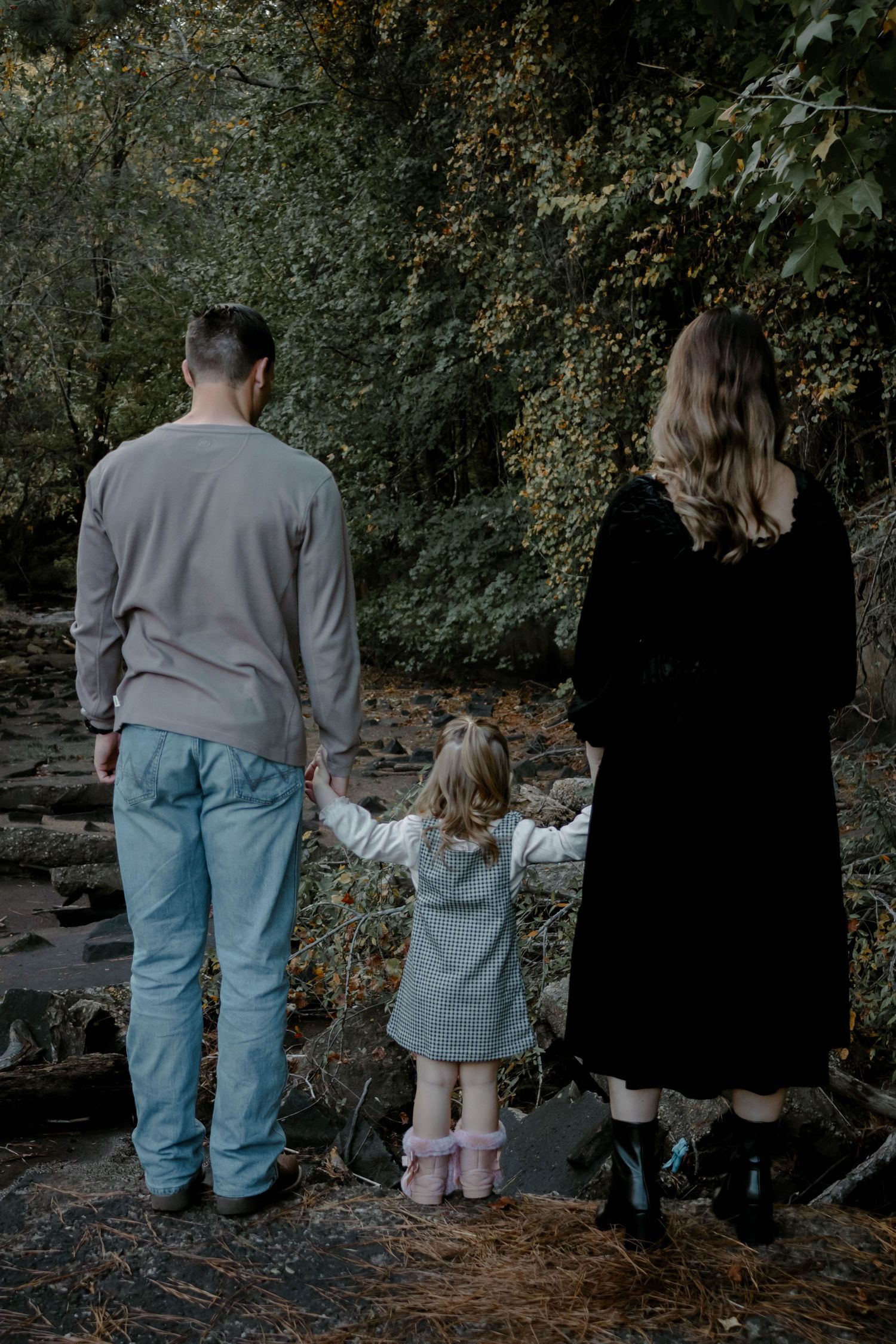 A group stands together at the edge of a wooded creek wearing casual clothing in muted tones.