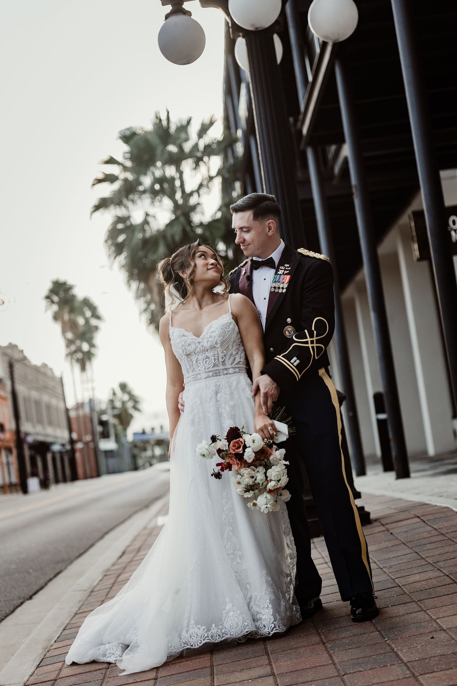 A newlywed couple poses together under white globe lights along an urban storefront.
