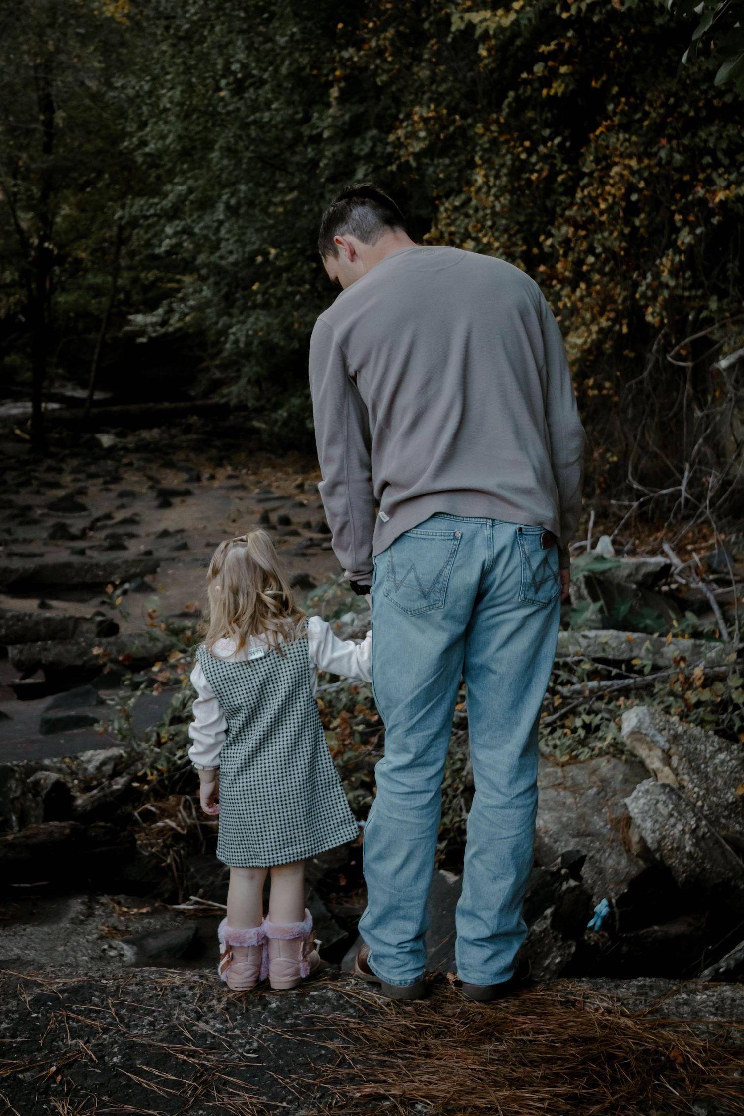 Two figures sit together on rocks by a stream in a moody forest setting during autumn.