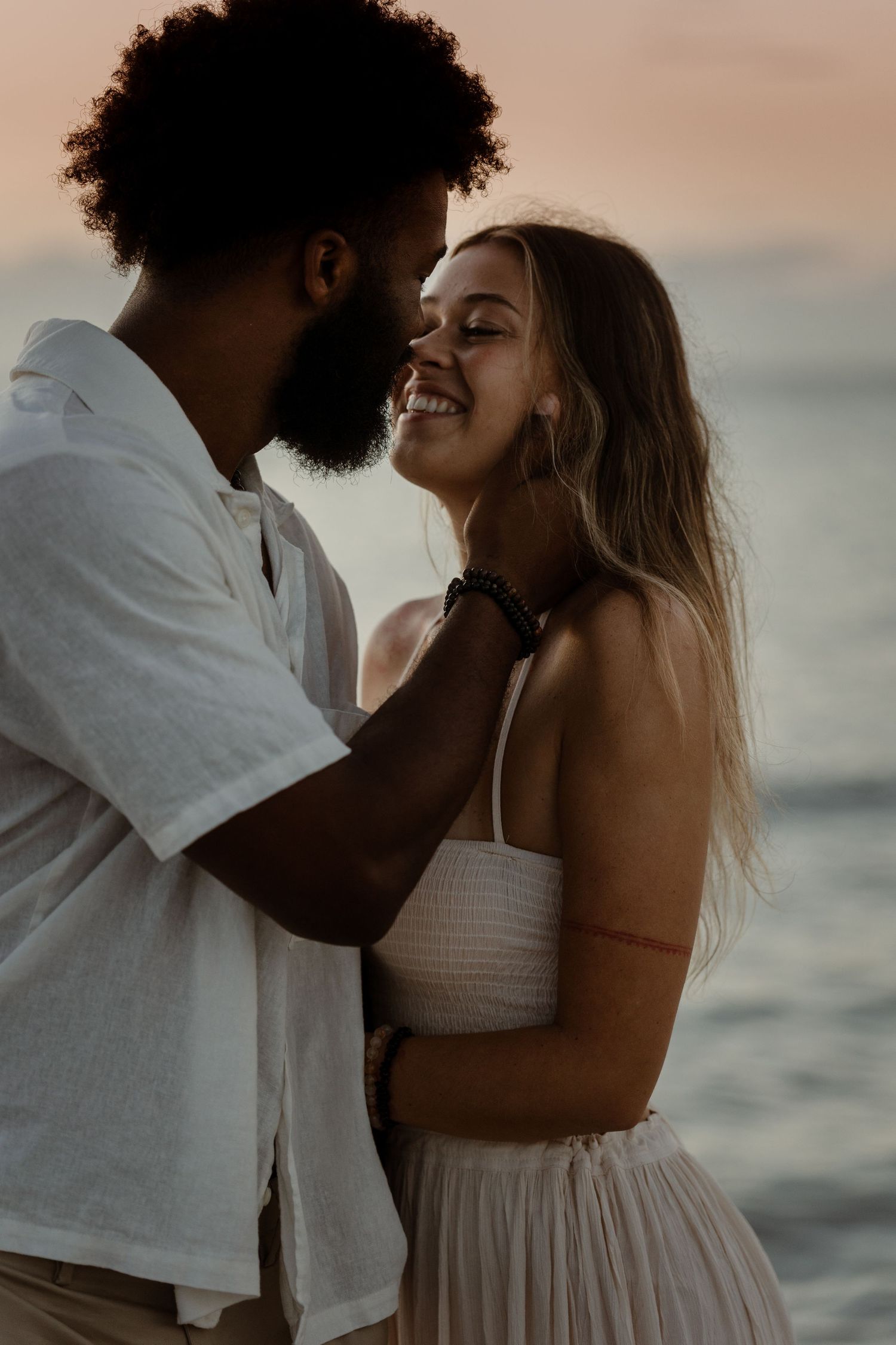 An intimate moment between a couple laughing together at sunset by the ocean.