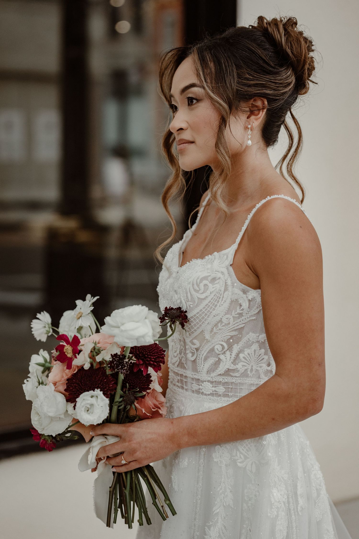 Wedding dress details showing intricate lace patterns and white floral bouquet with burgundy accents.