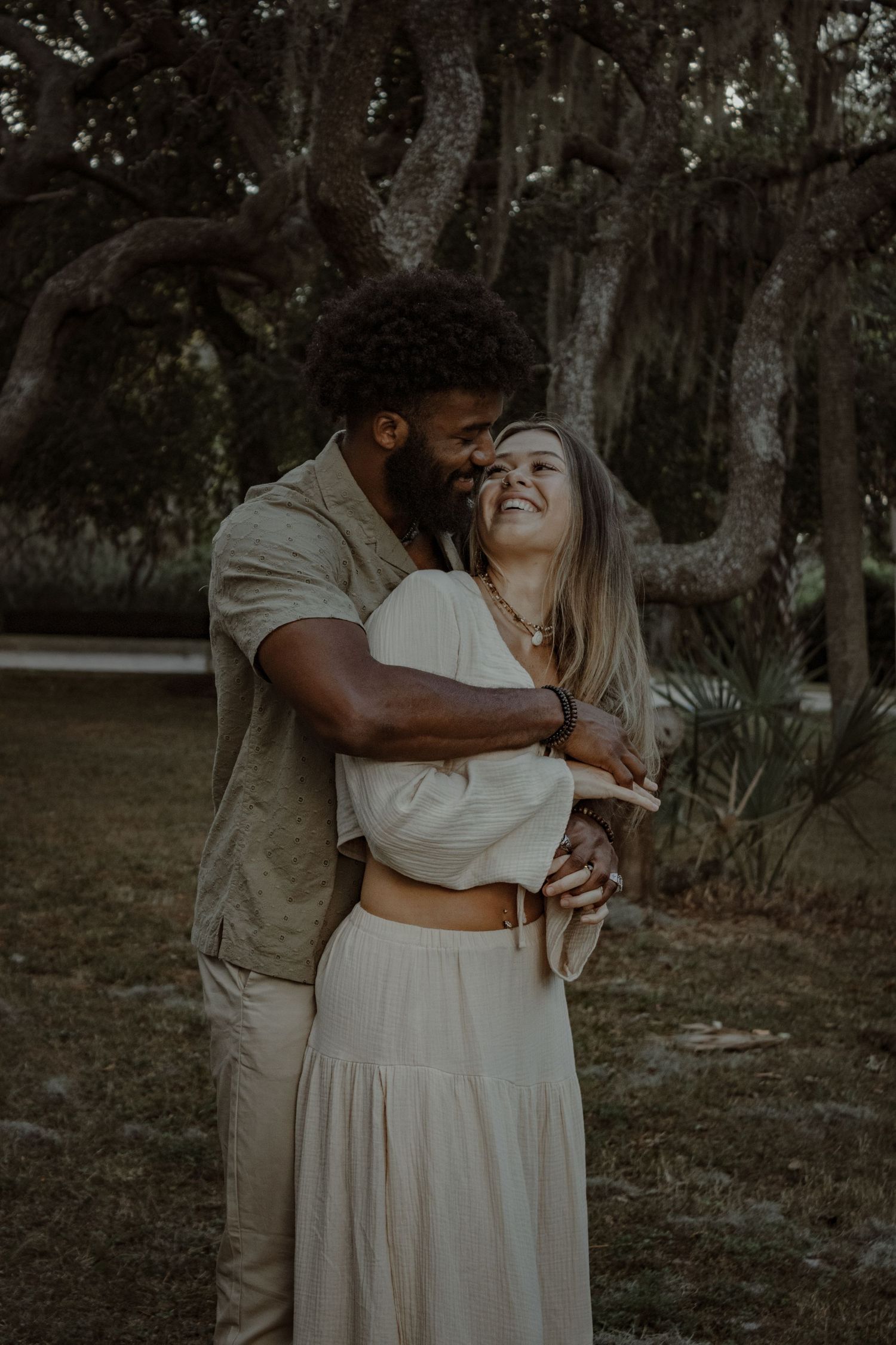 A loving embrace captured in a natural setting with Spanish moss and trees in the background.