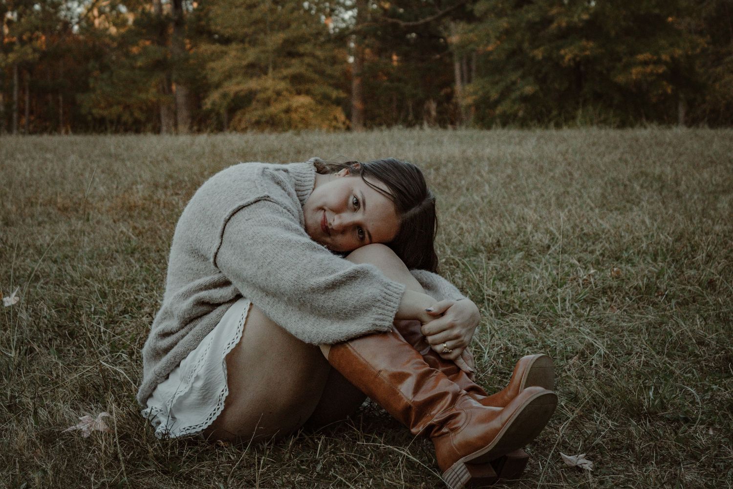 A couple embraces while lying in a grassy field during sunset, creating a romantic silhouette against the landscape.