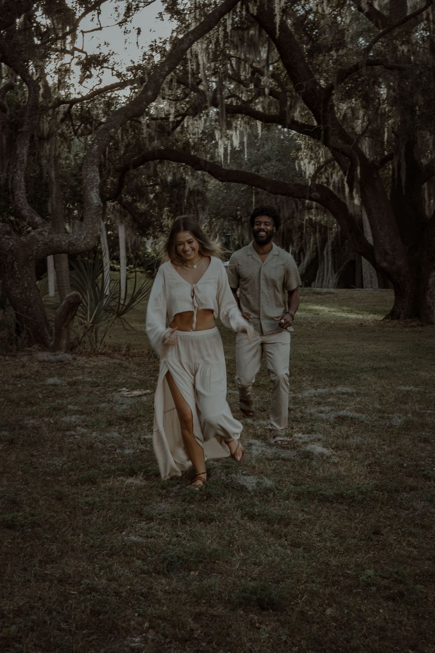 A romantic couple walks through a dreamy Spanish moss-covered forest setting.
