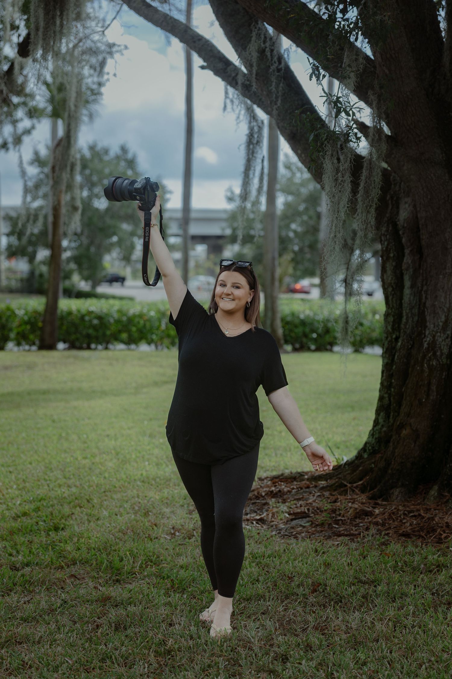 A dancer in black attire performs graceful movements under trees in a grassy outdoor setting.