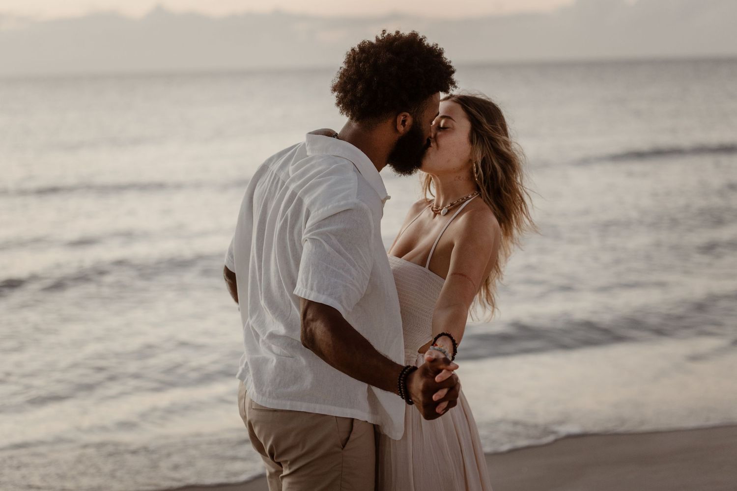 Romantic beach engagement photoshoot with couple embracing by the ocean at dusk.