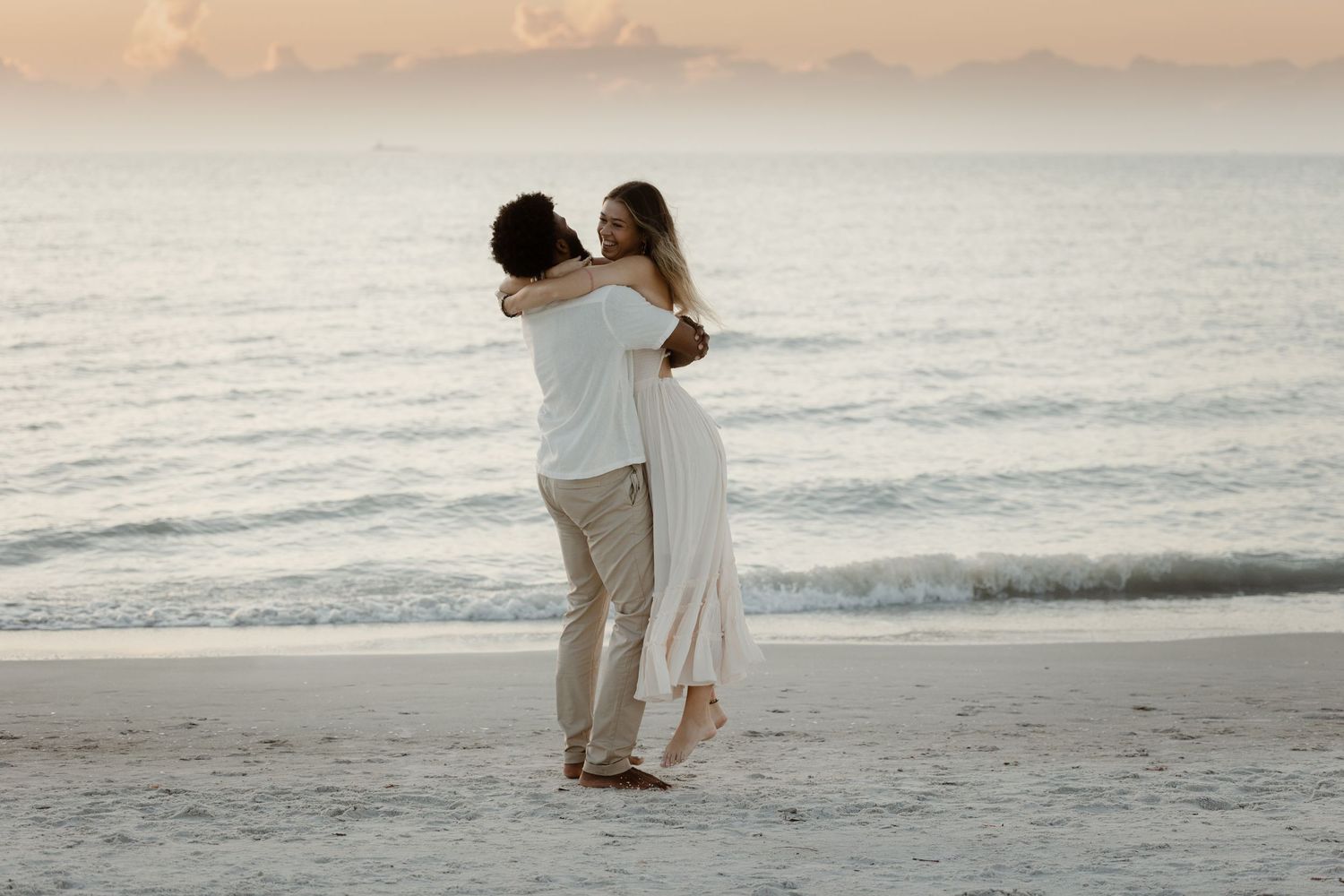 A romantic couple shares tender moments at sunset on a beautiful beach with gentle waves in the background.