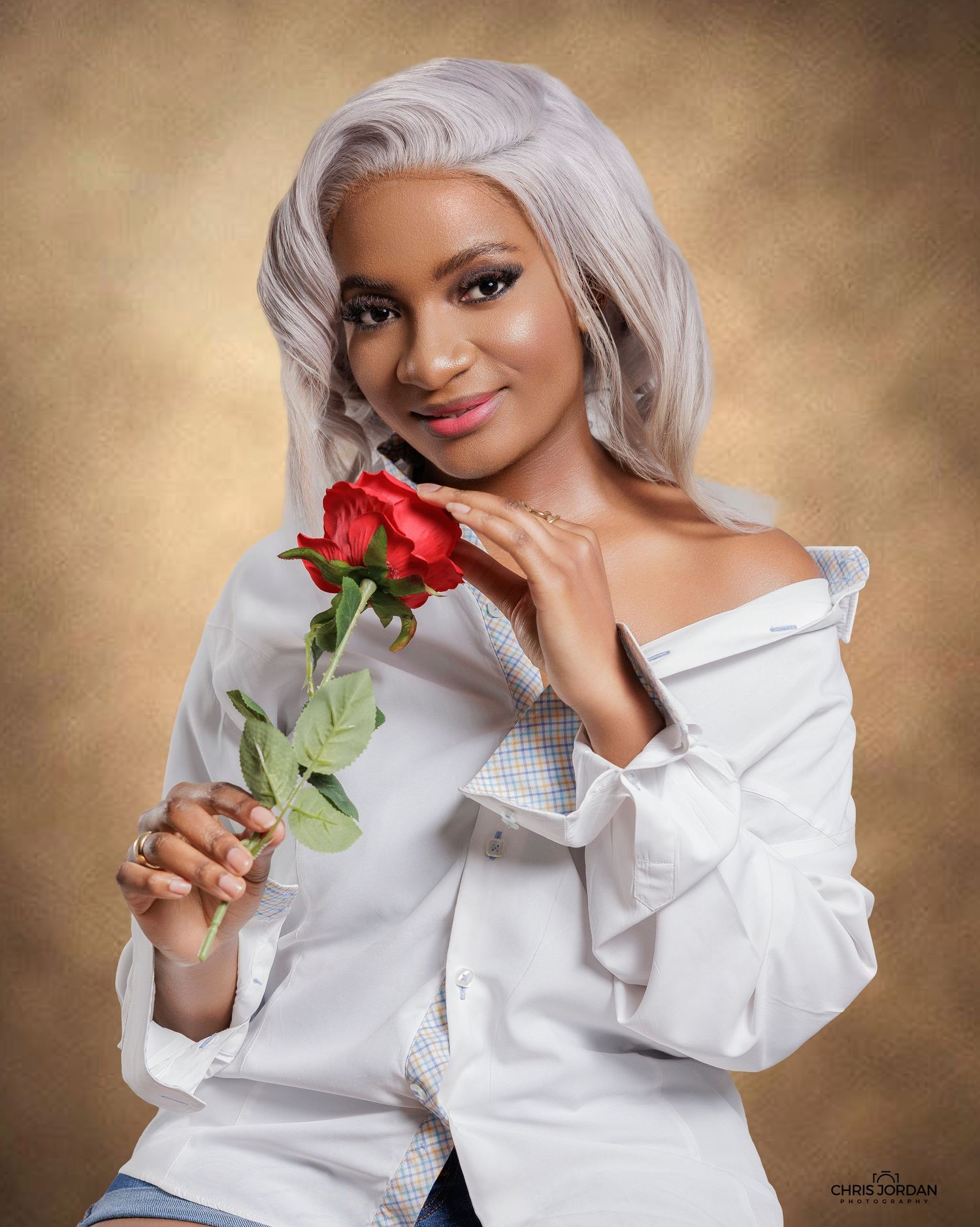 A woman in a white button-down shirt poses with a red rose against a golden brown background in a glamour portrait.