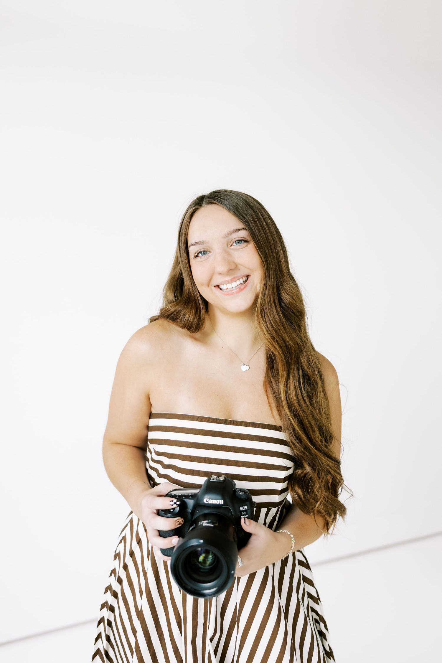Photographer in striped dress holding professional camera against white background.