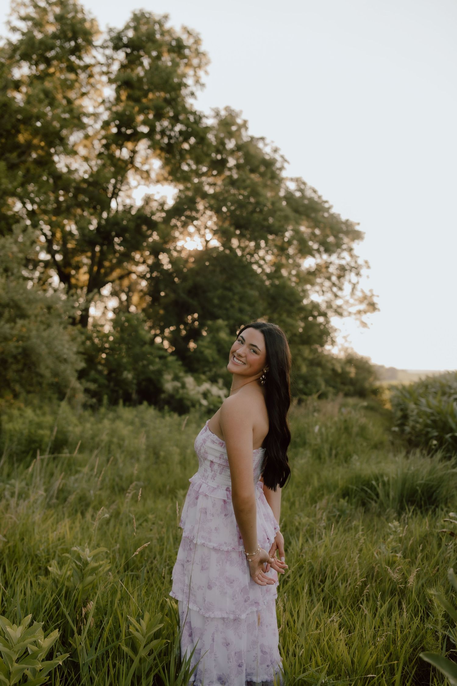 Outdoor portrait in a white tiered dress surrounded by tall grass at sunset.