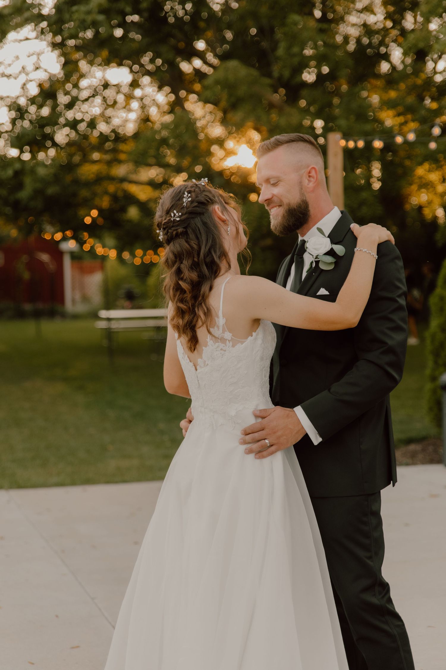 A romantic sunset wedding photo of newlyweds dancing outdoors with string lights in the background.