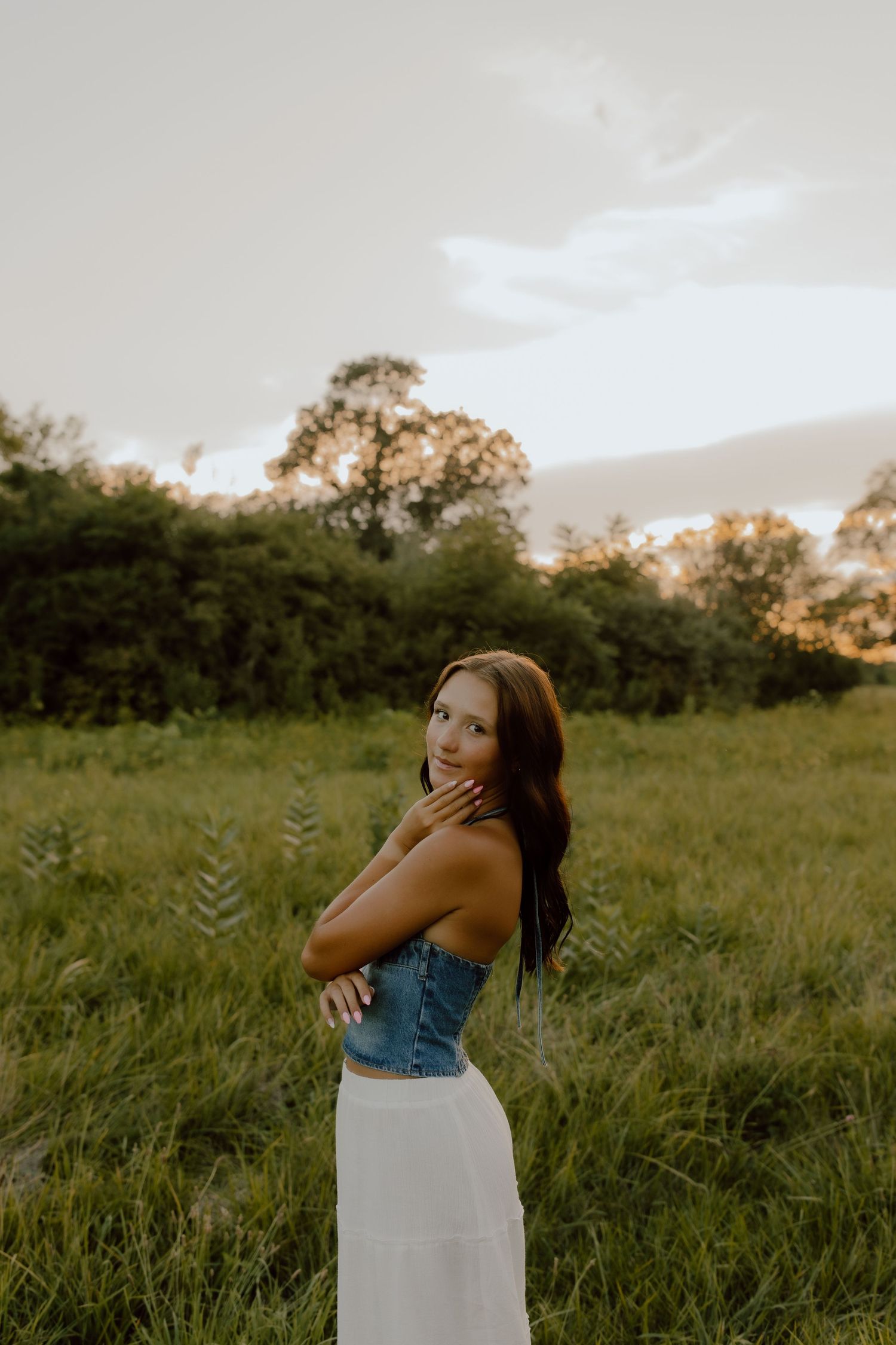 Summer portrait in denim and white skirt against golden hour meadow.