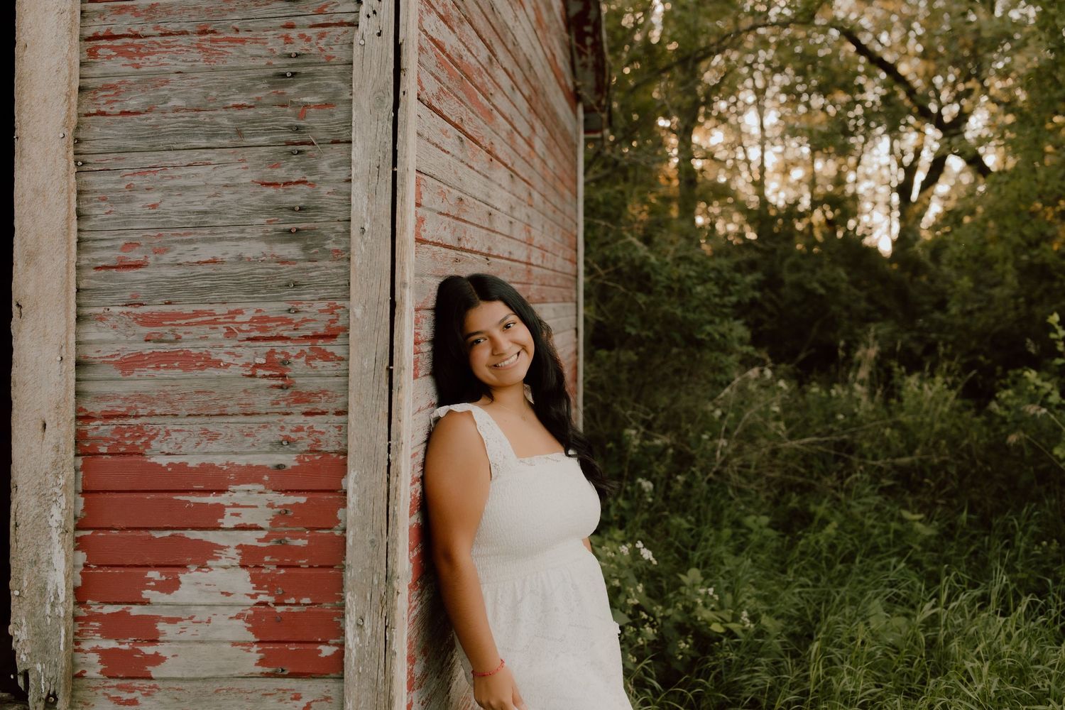 Portrait session against a weathered red barn wall during golden hour.