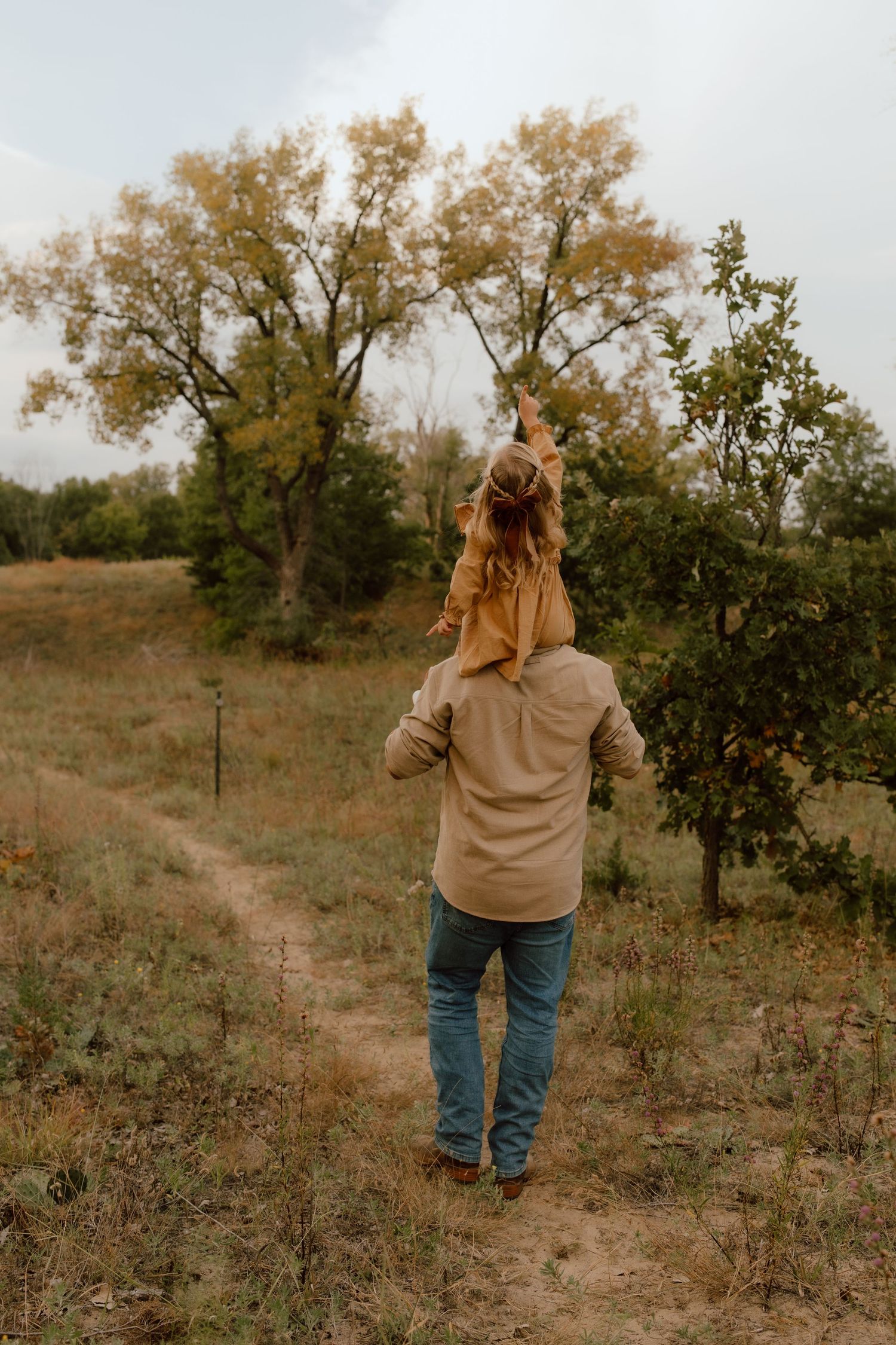 Person walking through an autumn orchard wearing a tan sweater and jeans in golden sunlight.