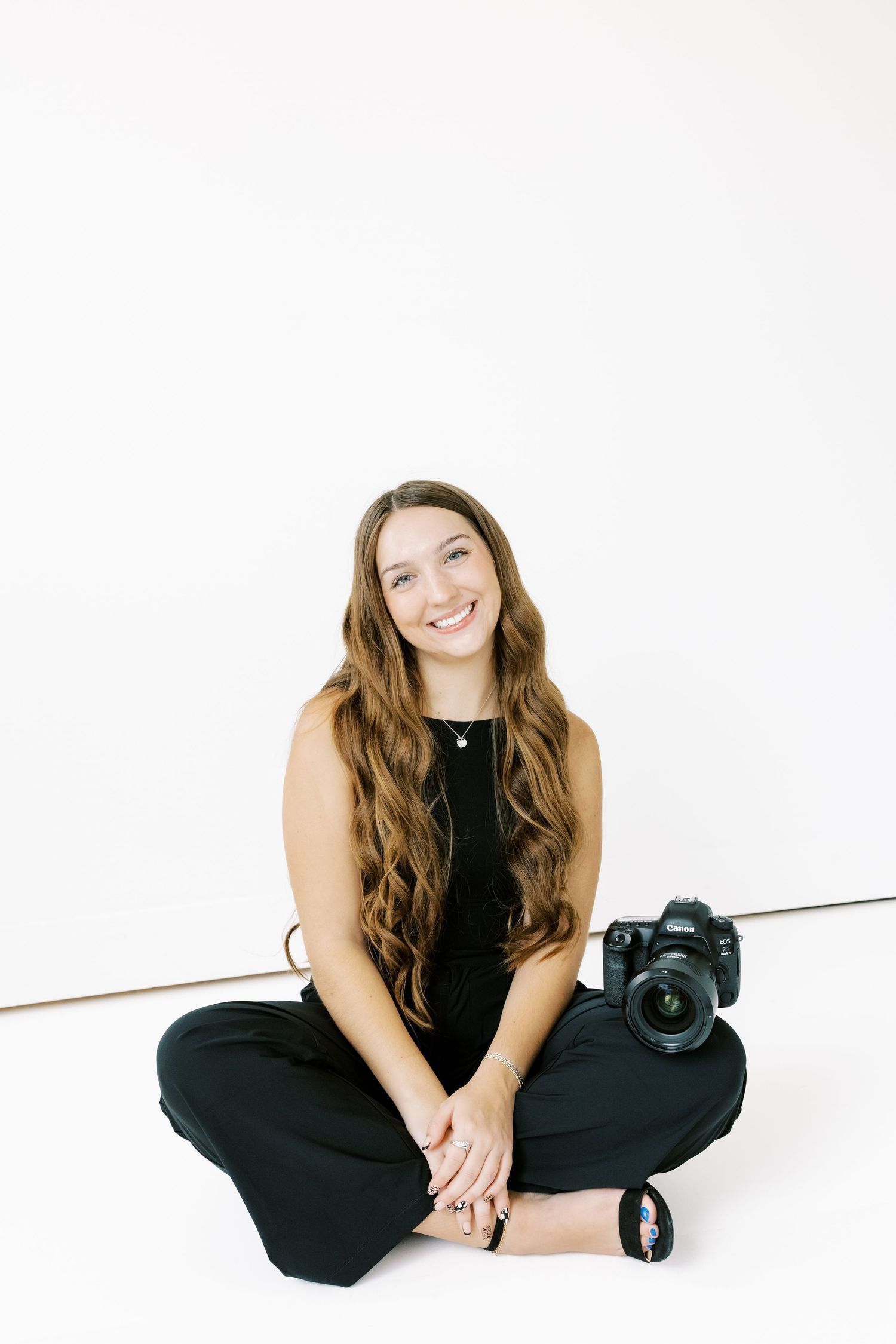 Professional photographer wearing black clothing poses with camera equipment against white background.