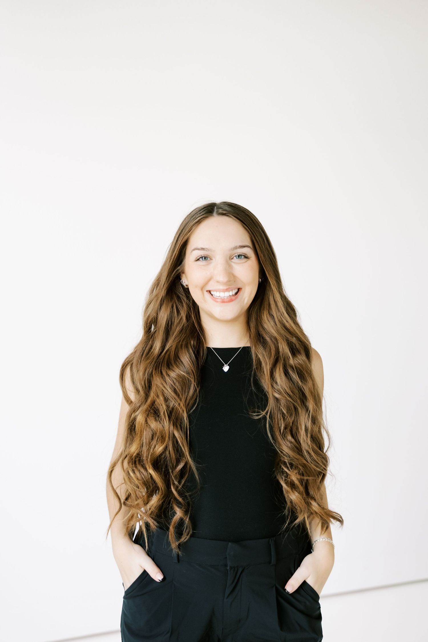 A person in a black outfit poses playfully against a white background.