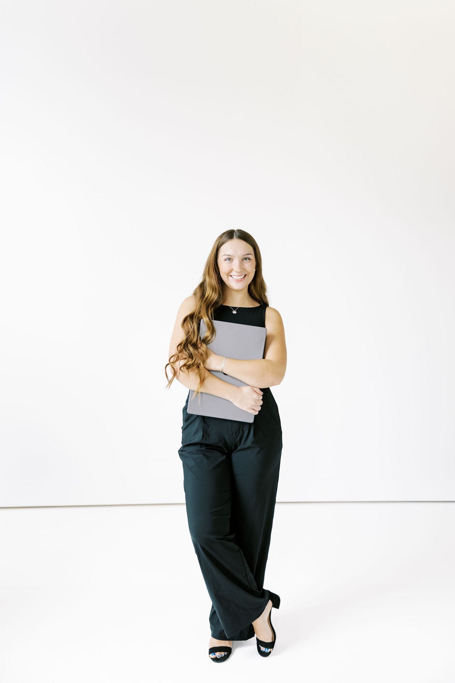 A person in black attire poses casually against a minimalist white studio background.