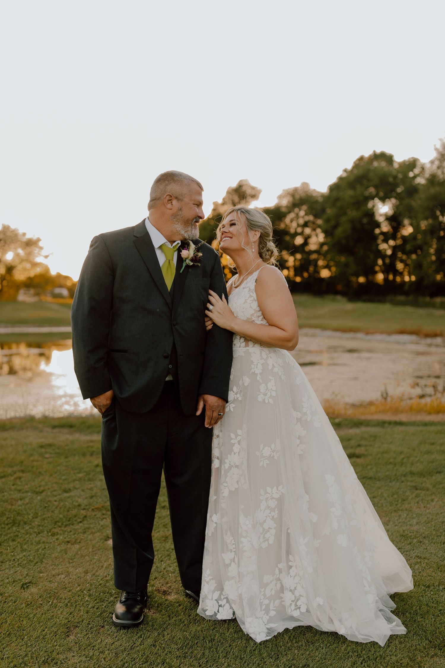 A joyful wedding couple shares a laugh during golden hour portraits on a golf course.