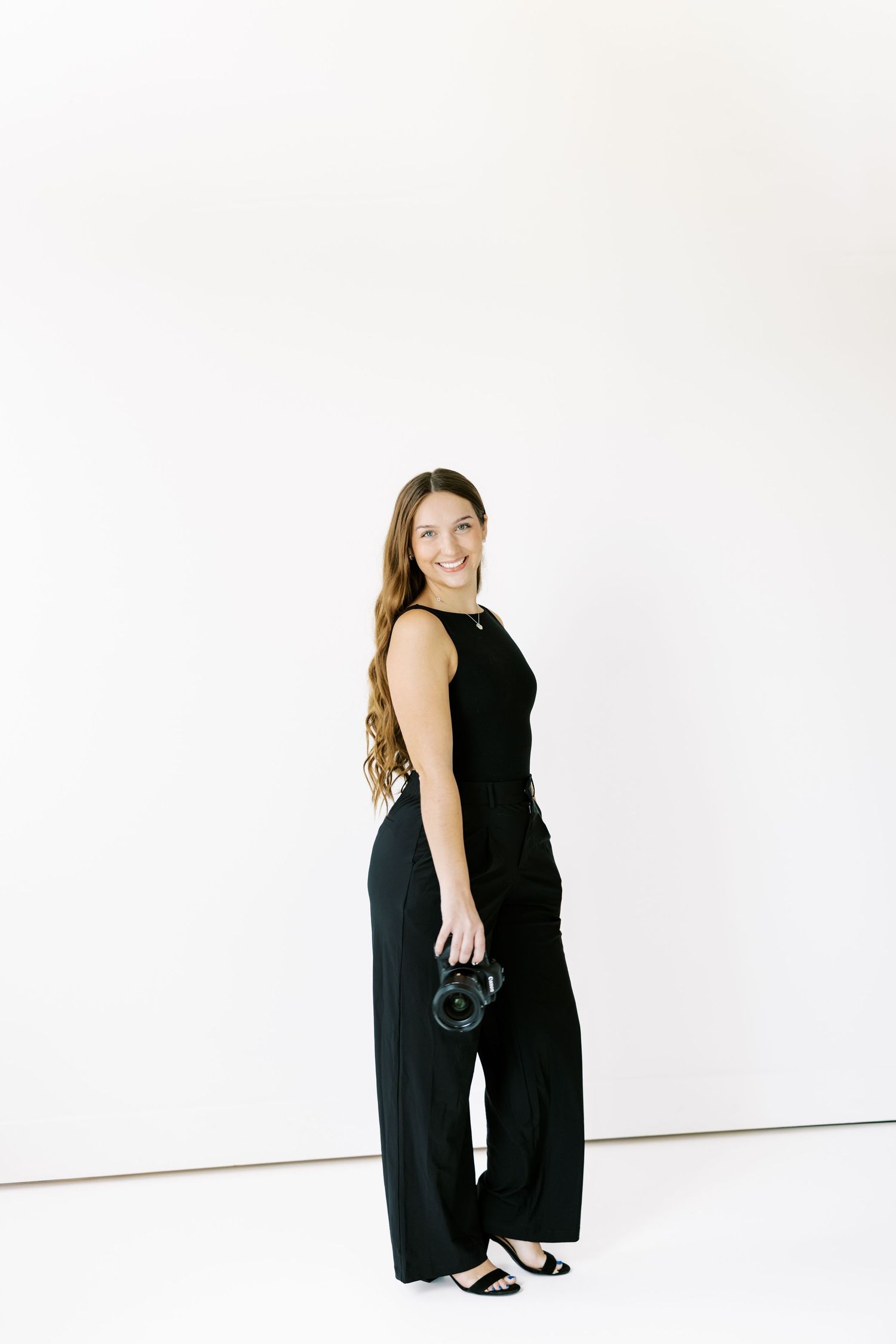 A figure in a black outfit poses gracefully against a white studio backdrop.