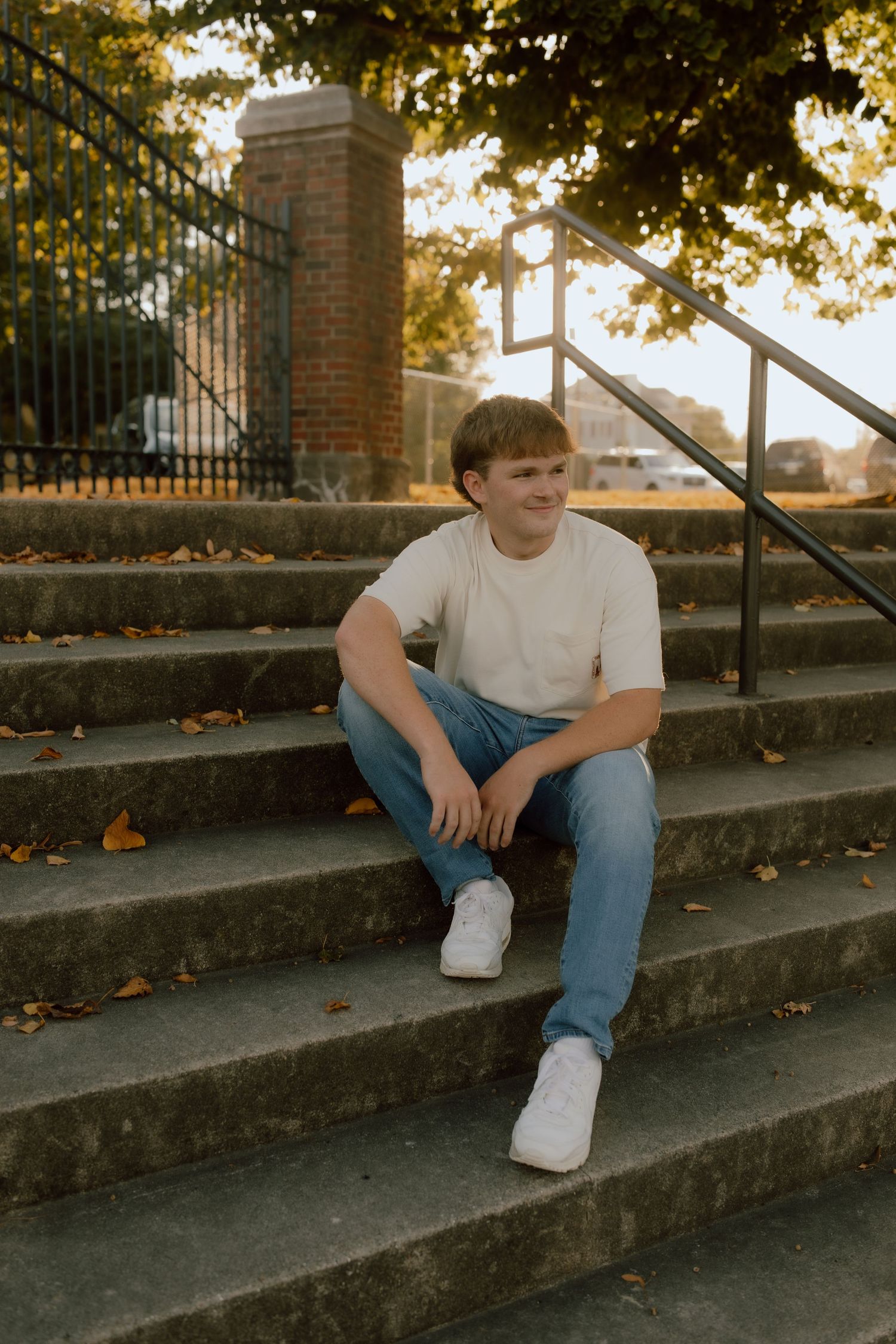 Figure sits casually on concrete steps surrounded by autumn leaves and golden sunlight.