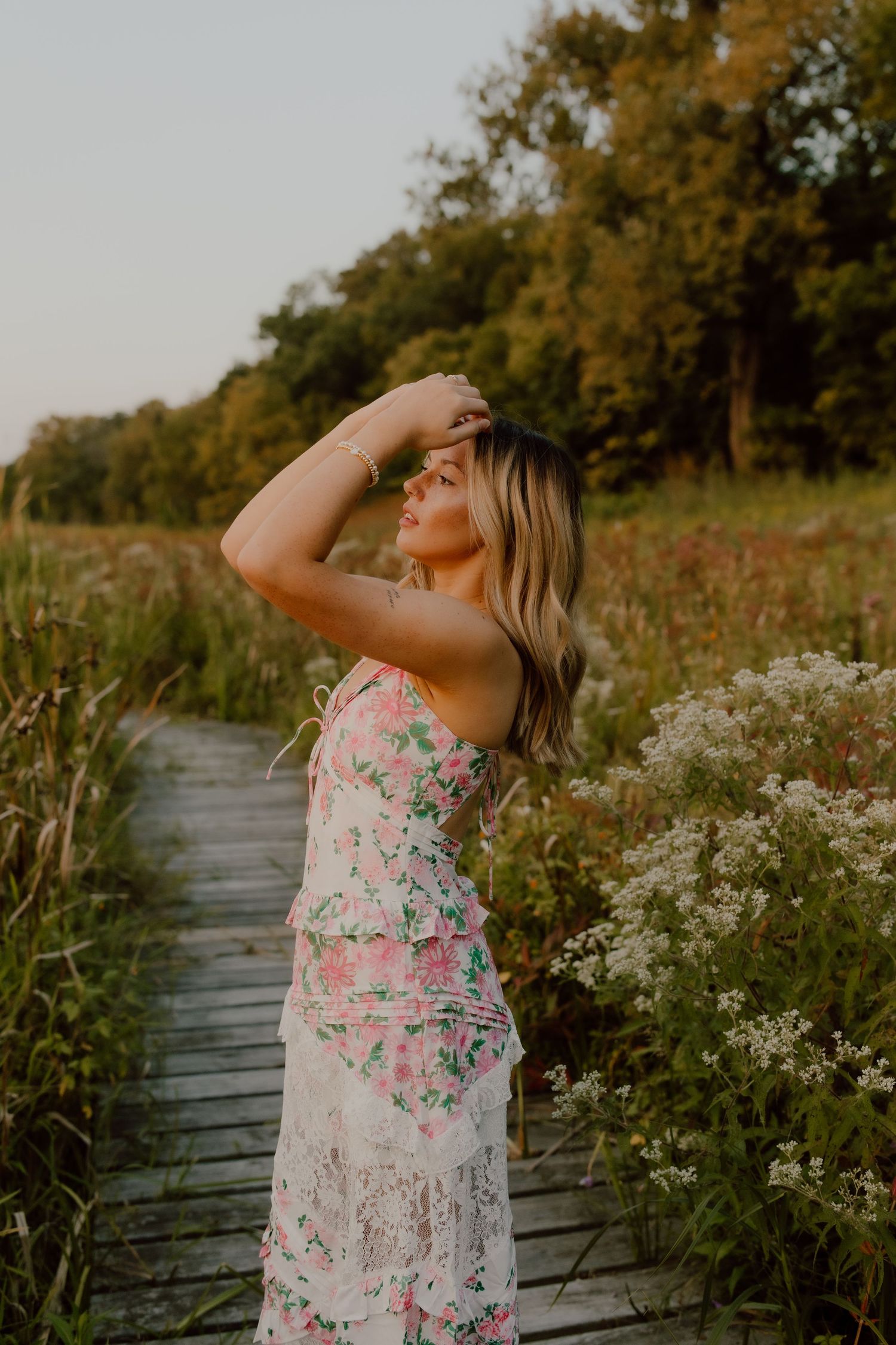 Dreamy portrait session among white wildflowers along a wooden boardwalk at sunset.