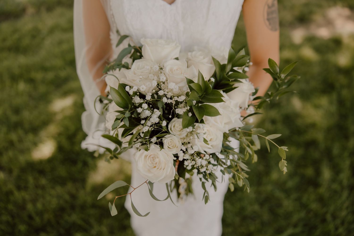Bride holding a lush white floral bouquet with greenery and baby's breath on her wedding day.