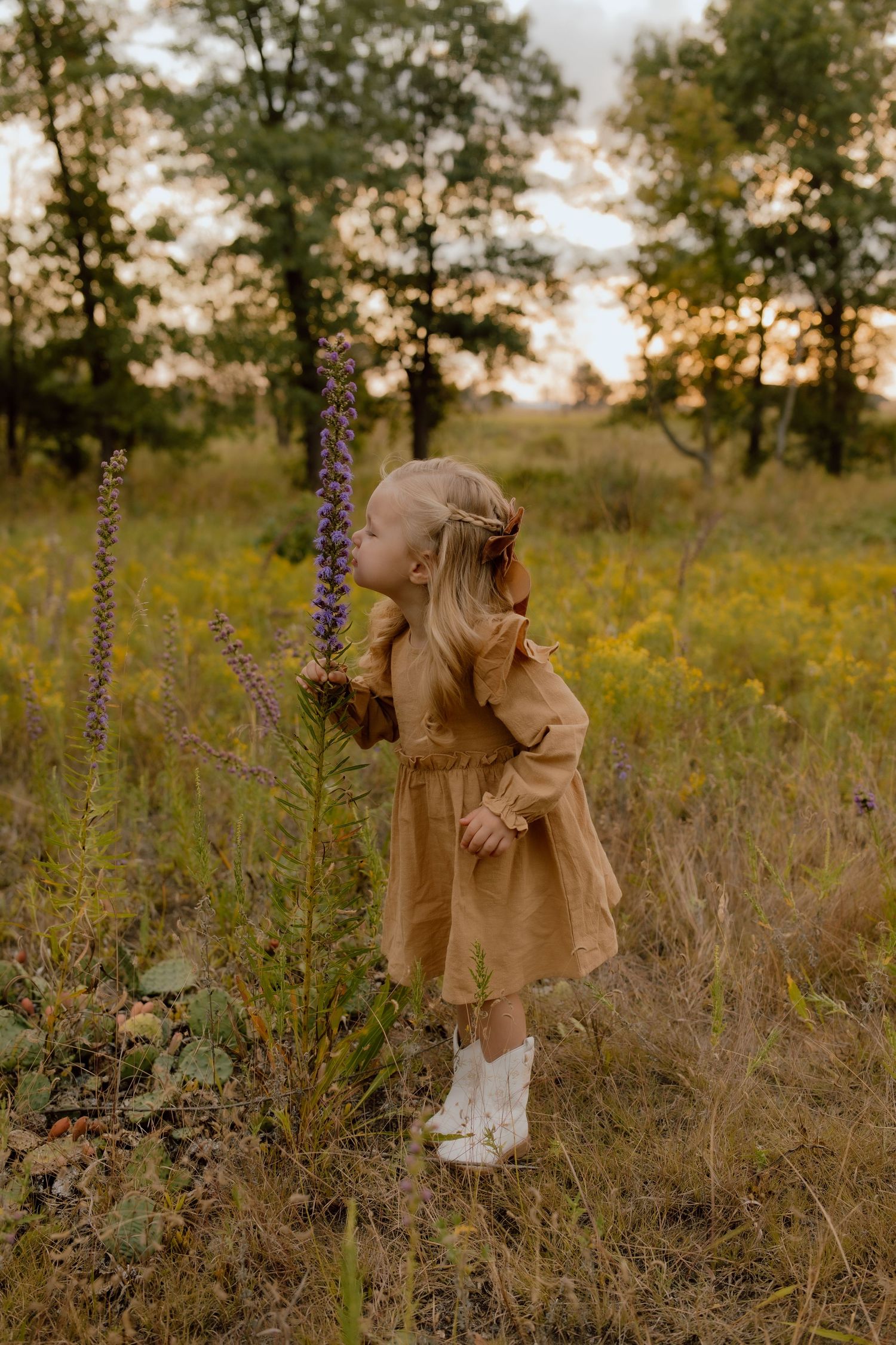 A small child in a tan coat explores a field of wildflowers at sunset.
