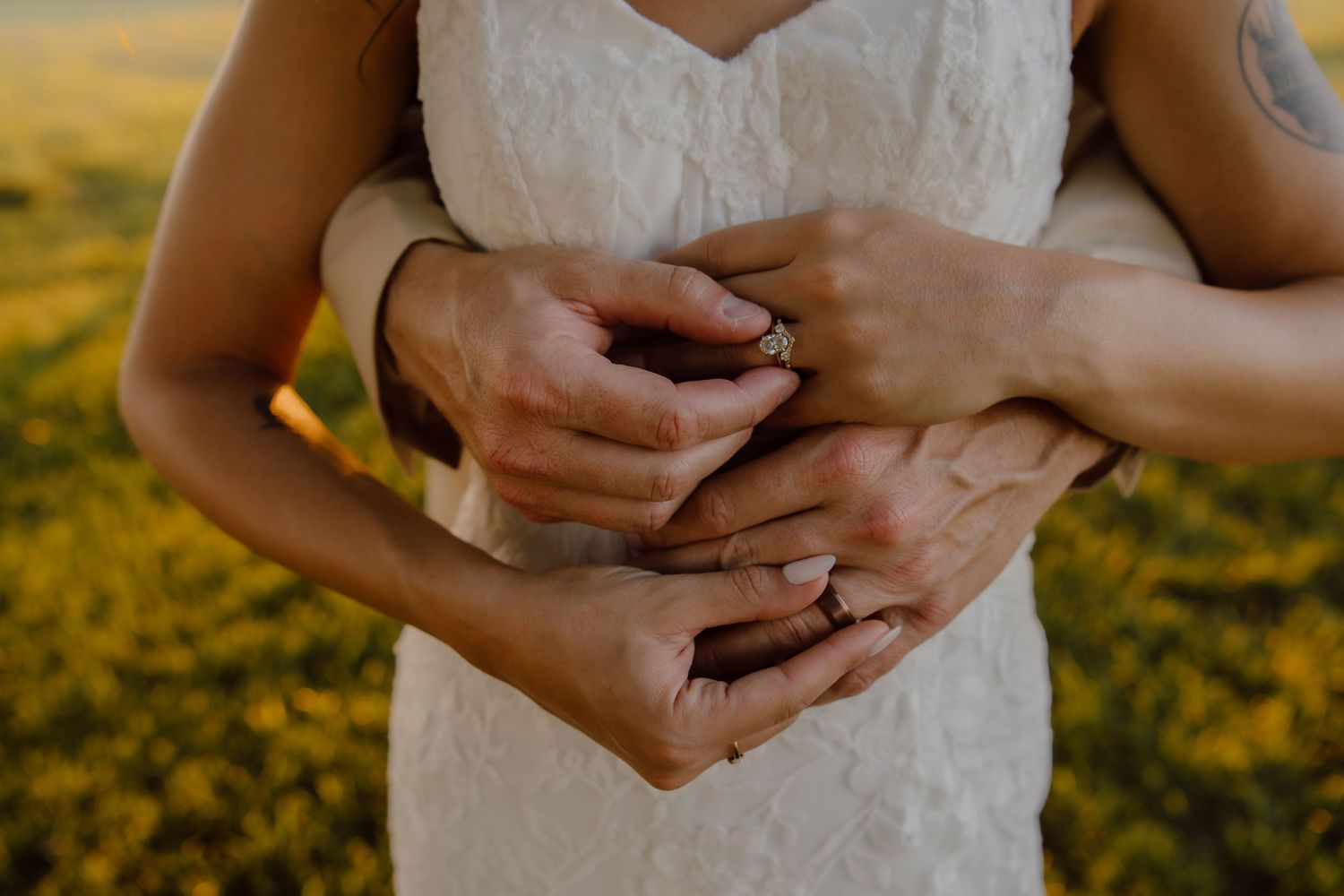 Close-up of newlyweds hands with wedding rings embracing in a sunny field.