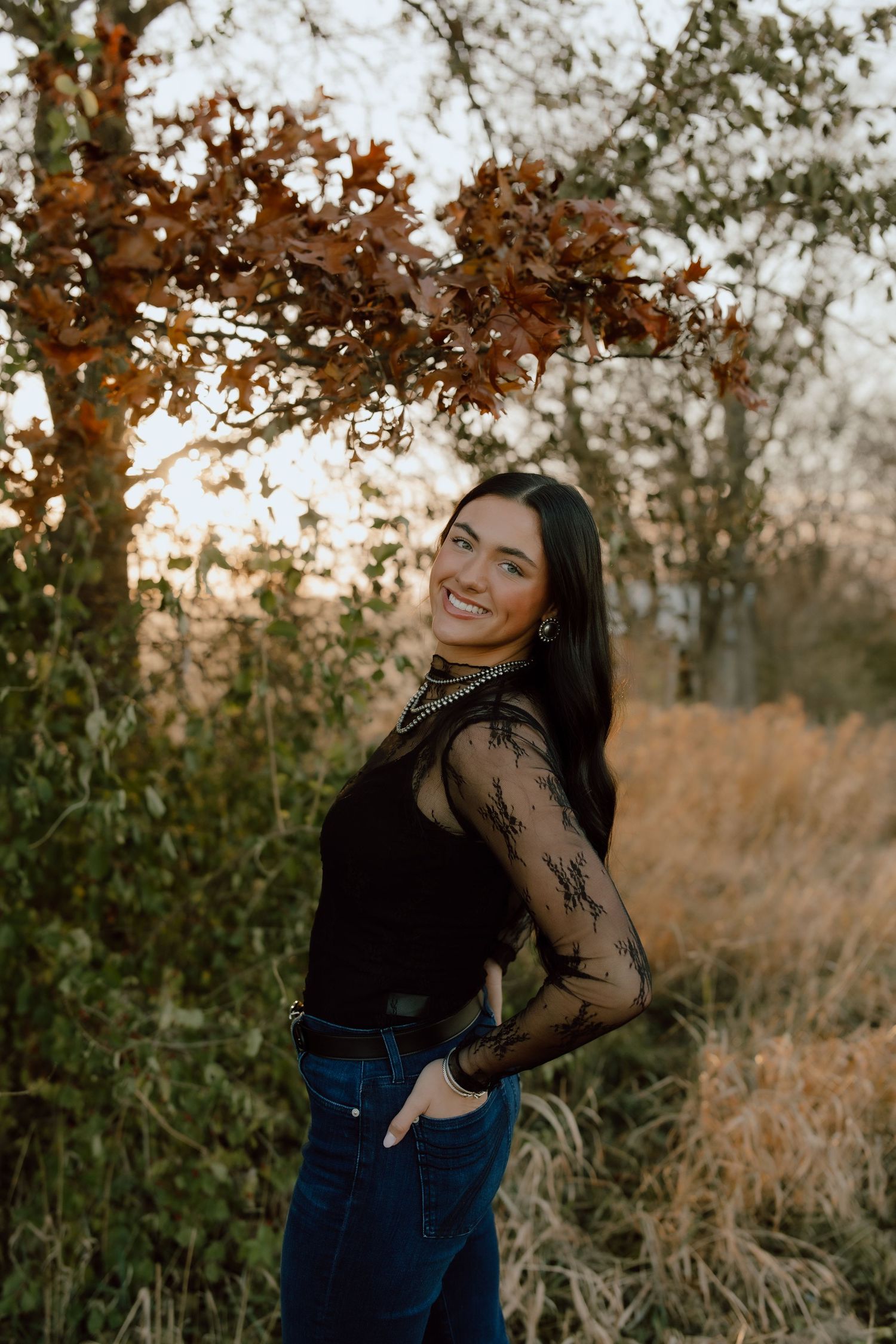 A portrait in a black lace top against autumn foliage at golden hour.