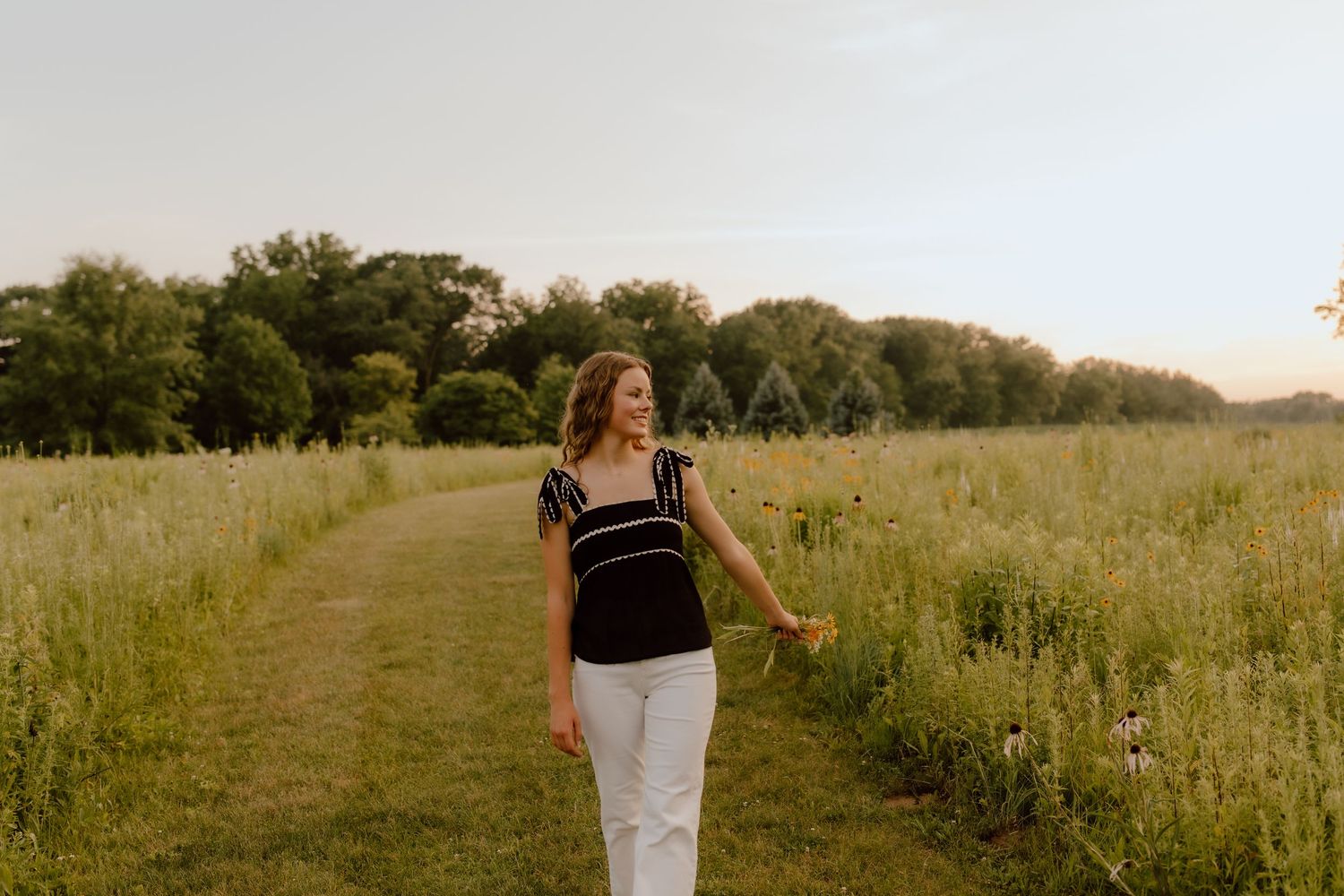 Figure walking along a dirt path through a serene meadow at dusk.