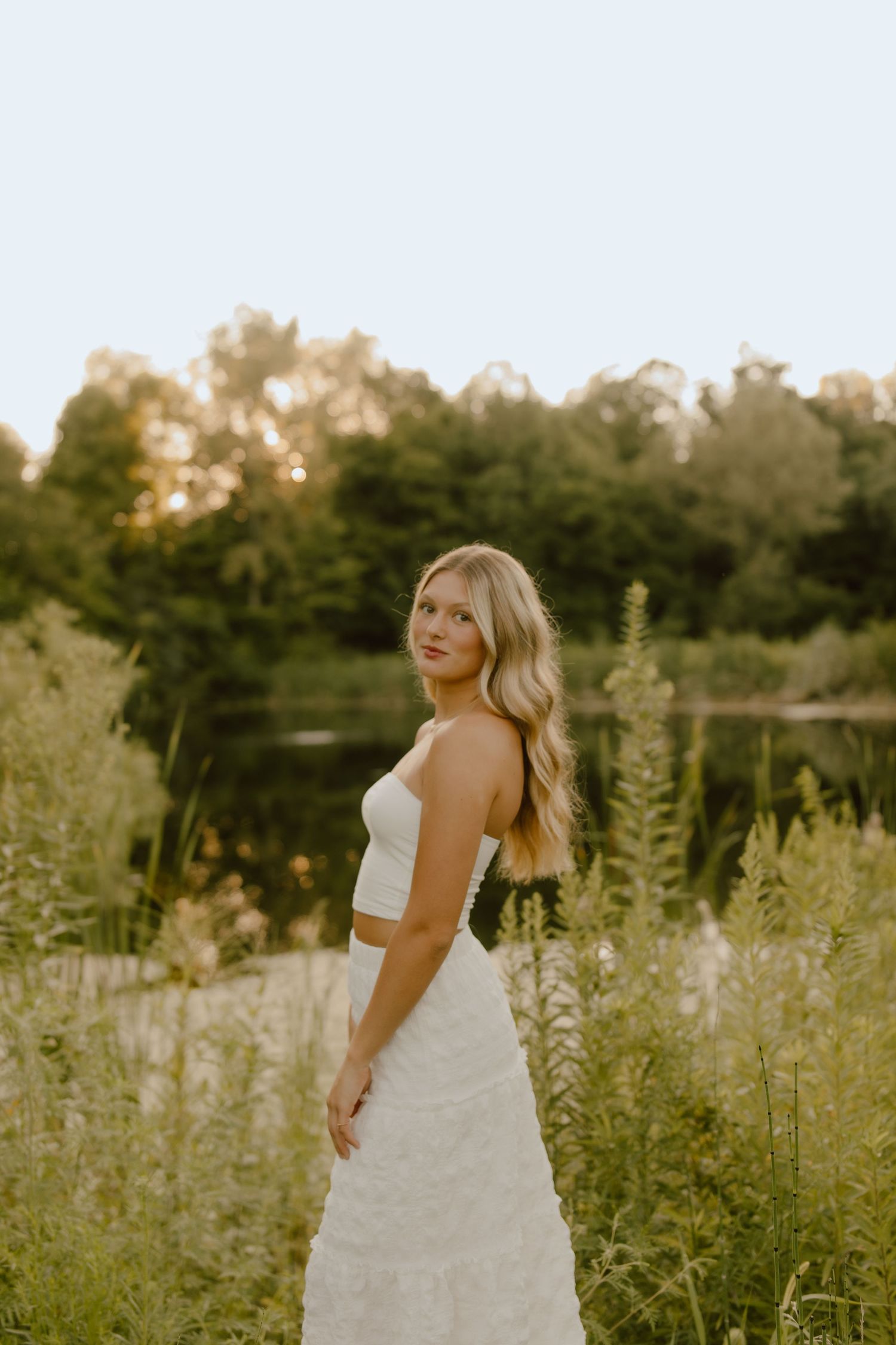 Romantic outdoor portrait session in white dress among wildflowers at sunset.