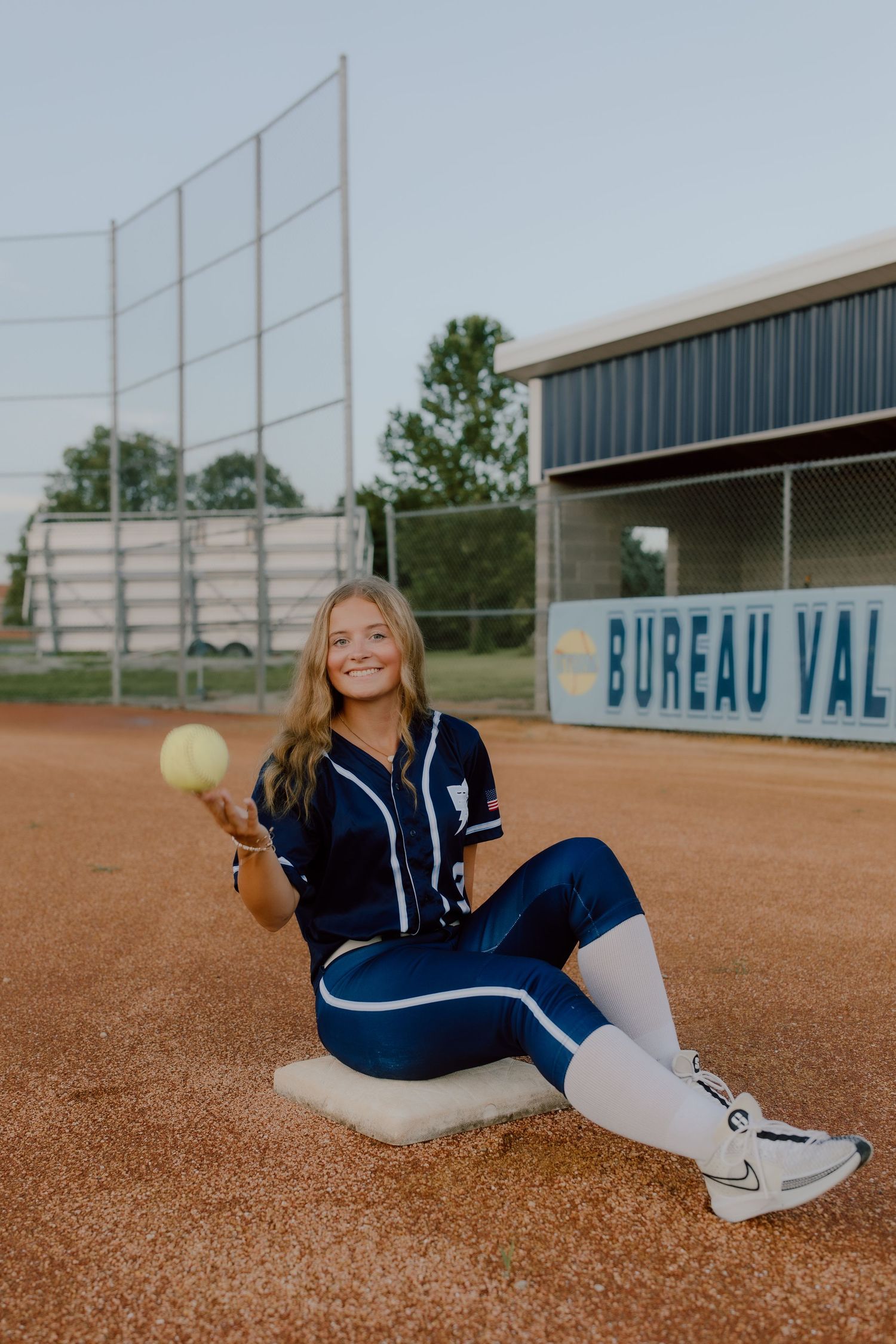 Softball player in uniform sitting on field with ball at Bureau Valley.