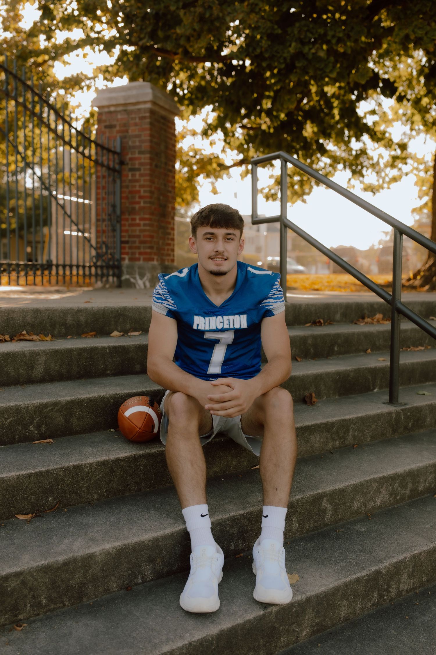 Athletic portrait session on concrete steps featuring blue football uniform and equipment.