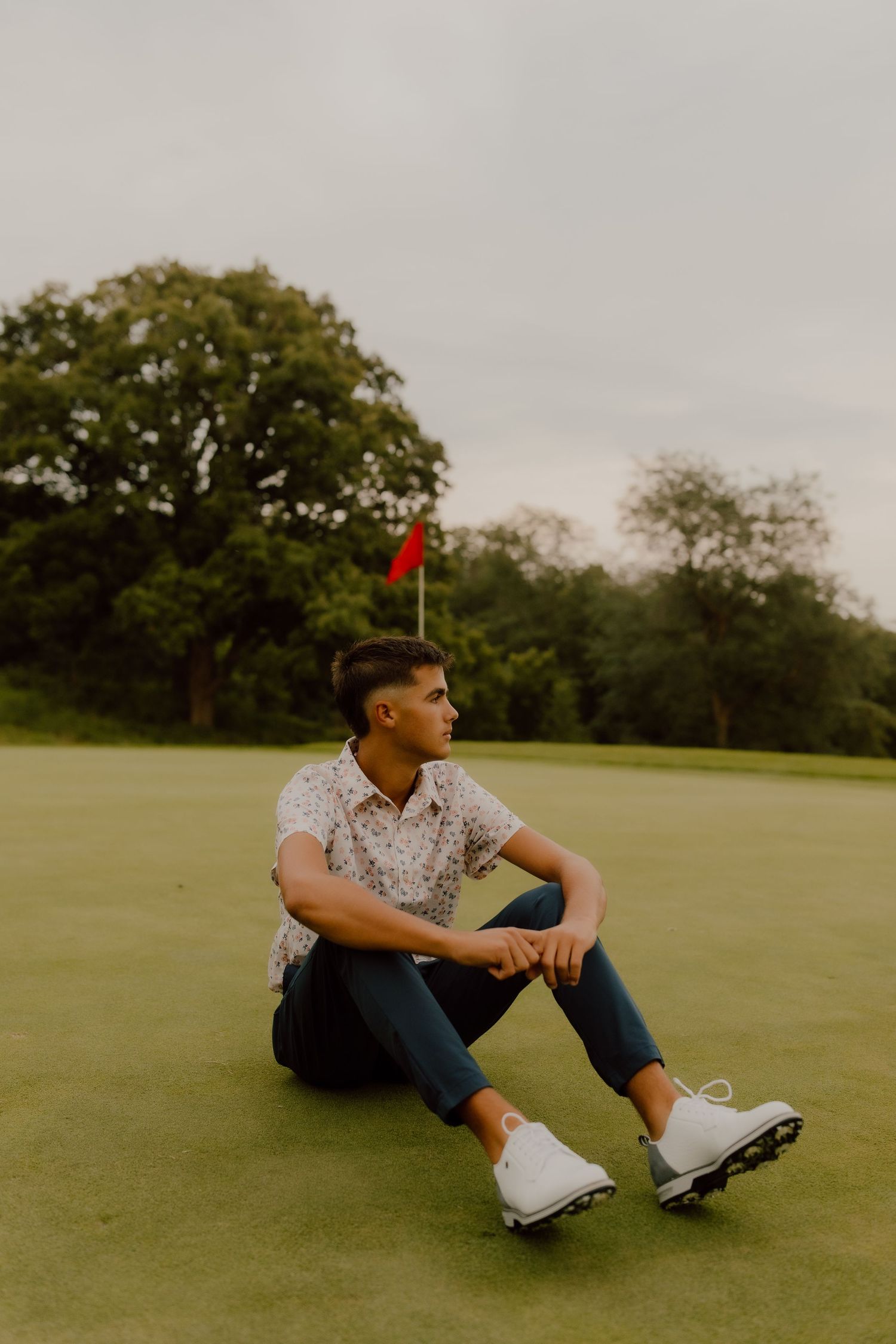 Casual golfer sitting on putting green wearing patterned shirt and jeans.