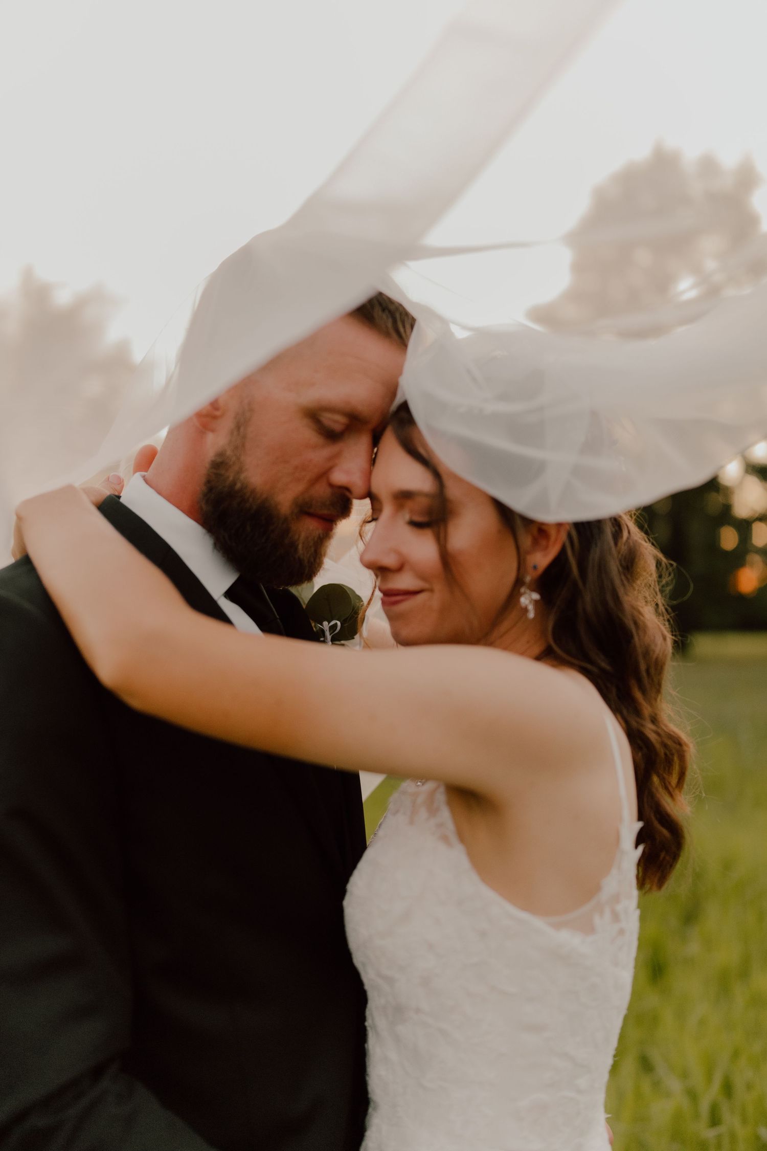 A tender moment between newlyweds as the bride's veil flows in the golden sunset light.