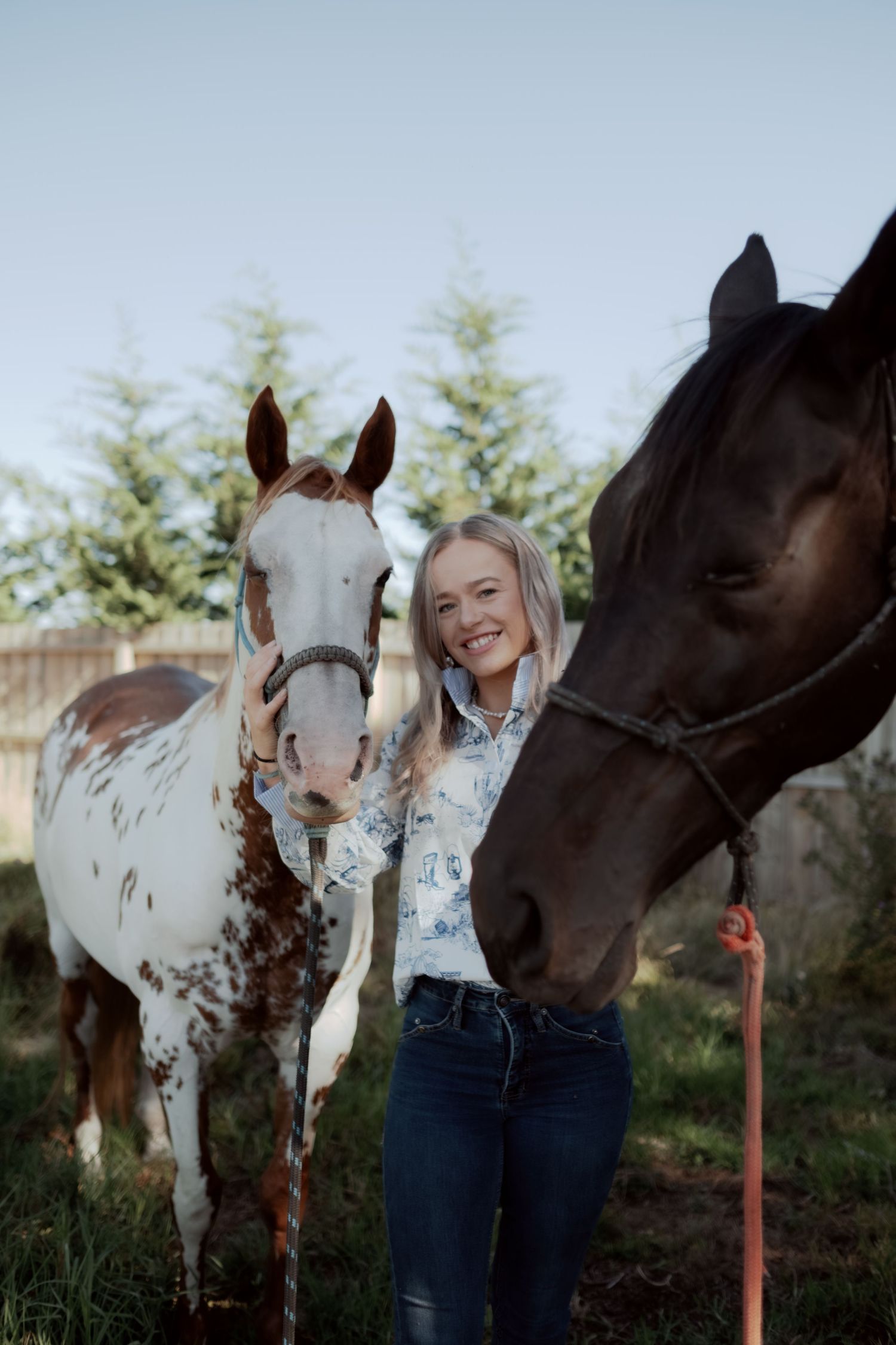 Warrnambool photographer captures smiling blonde woman posing with a paint horse and dark horse outdoors.