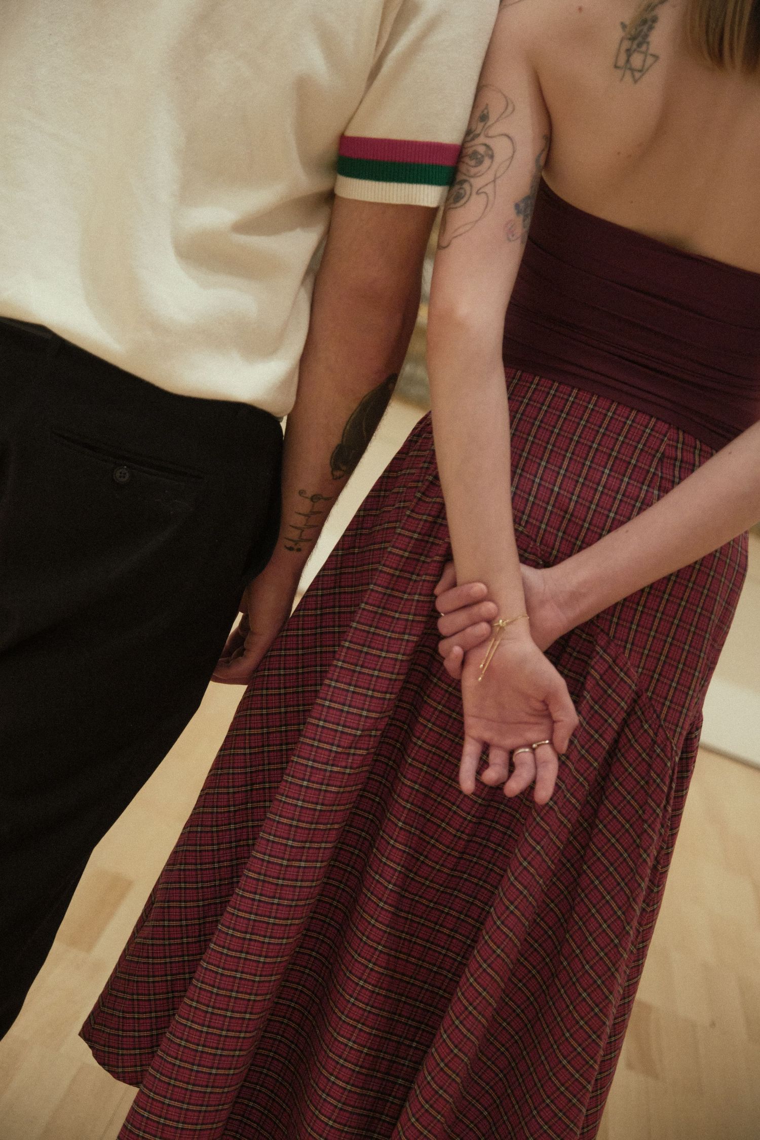 Close-up of a couple holding hands, showing tattoos and a plaid skirt in a romantic moment.