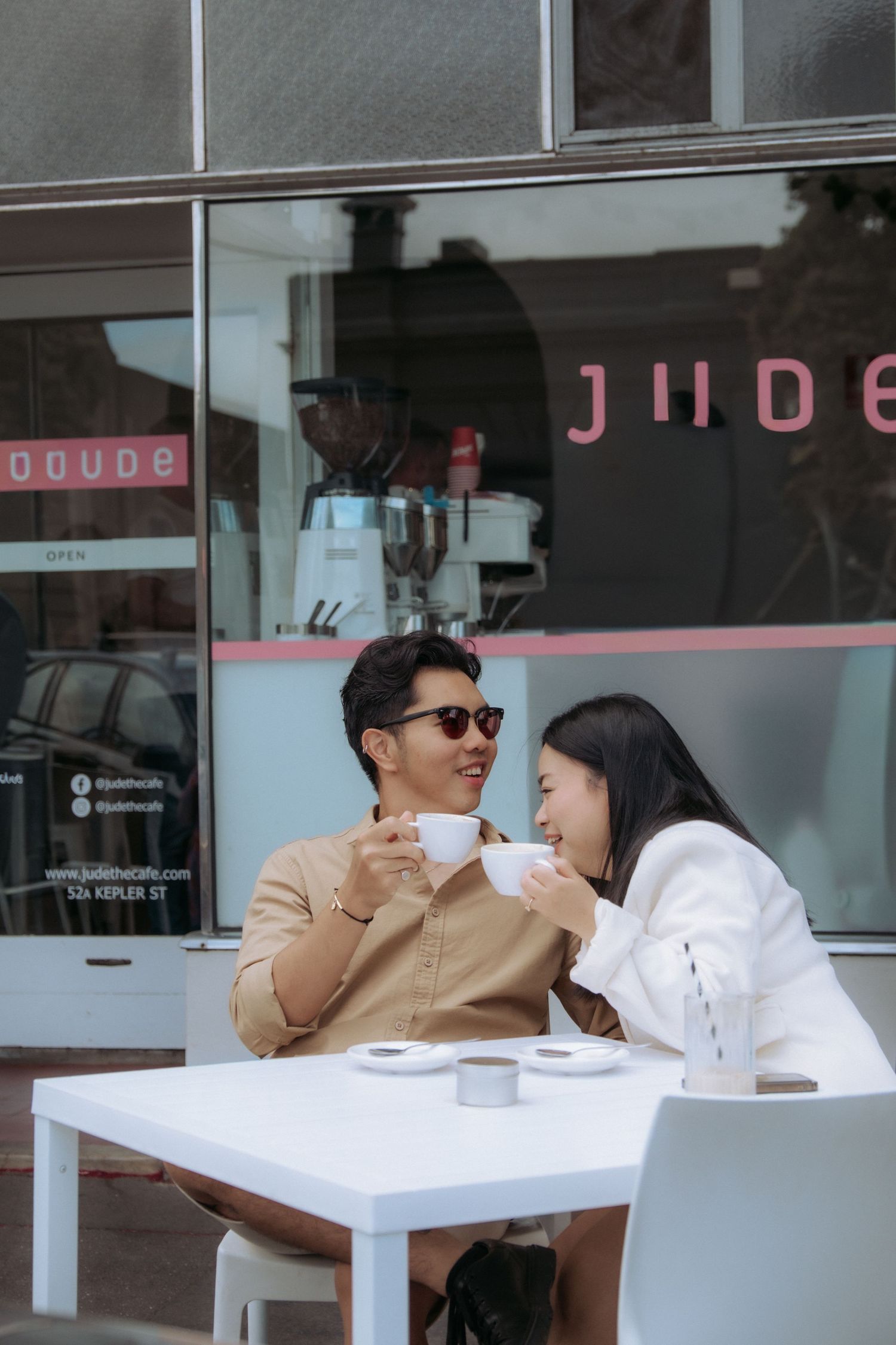Couple sharing coffee and smiling at each other at an outdoor cafe table captured by Visuals By Dani Warrnambool photographer