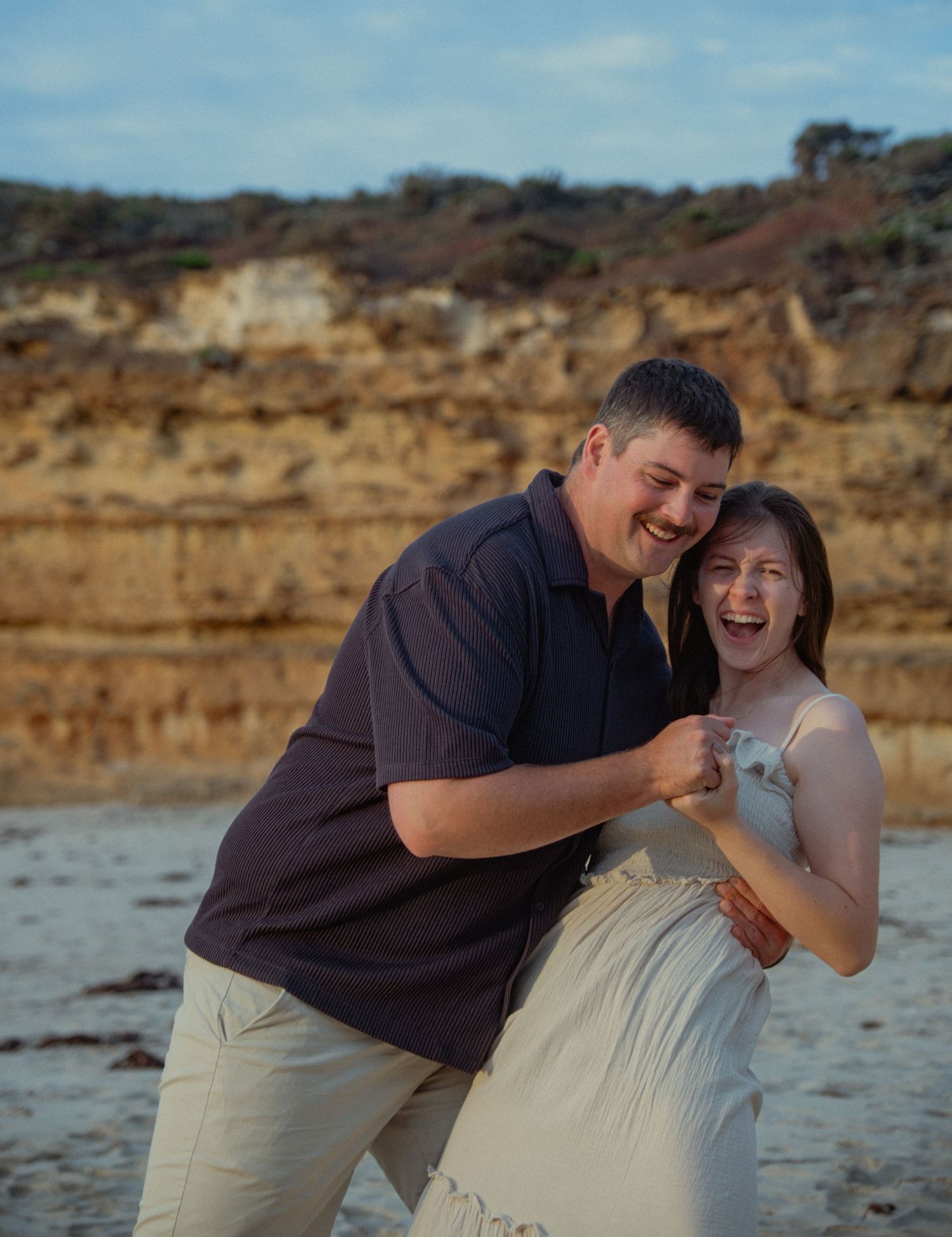 Laughing couple embracing on a sandy beach with golden cliffs in the background near Warrnambool.
