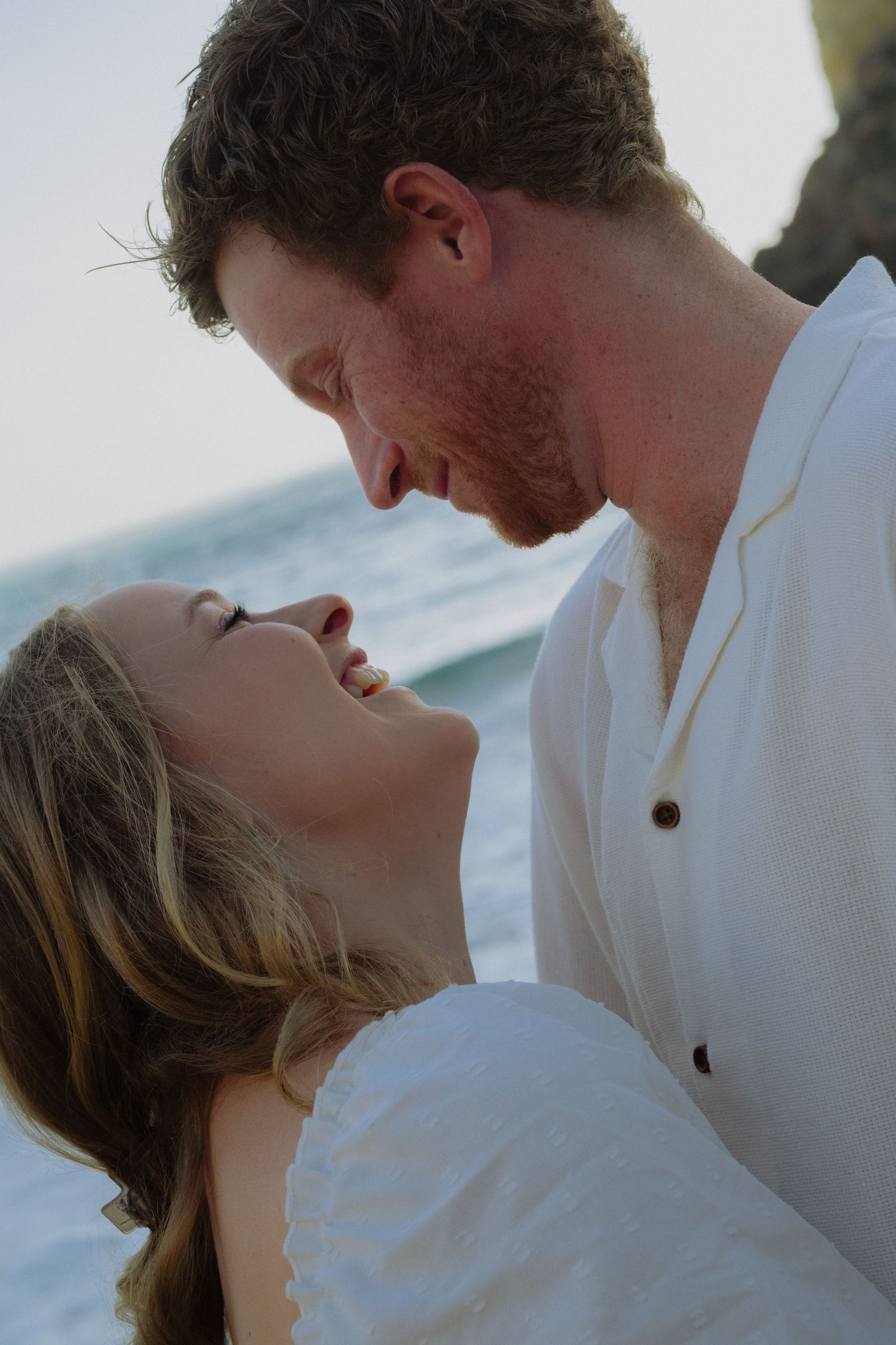 Romantic couple sharing an intimate moment laughing together near the ocean.