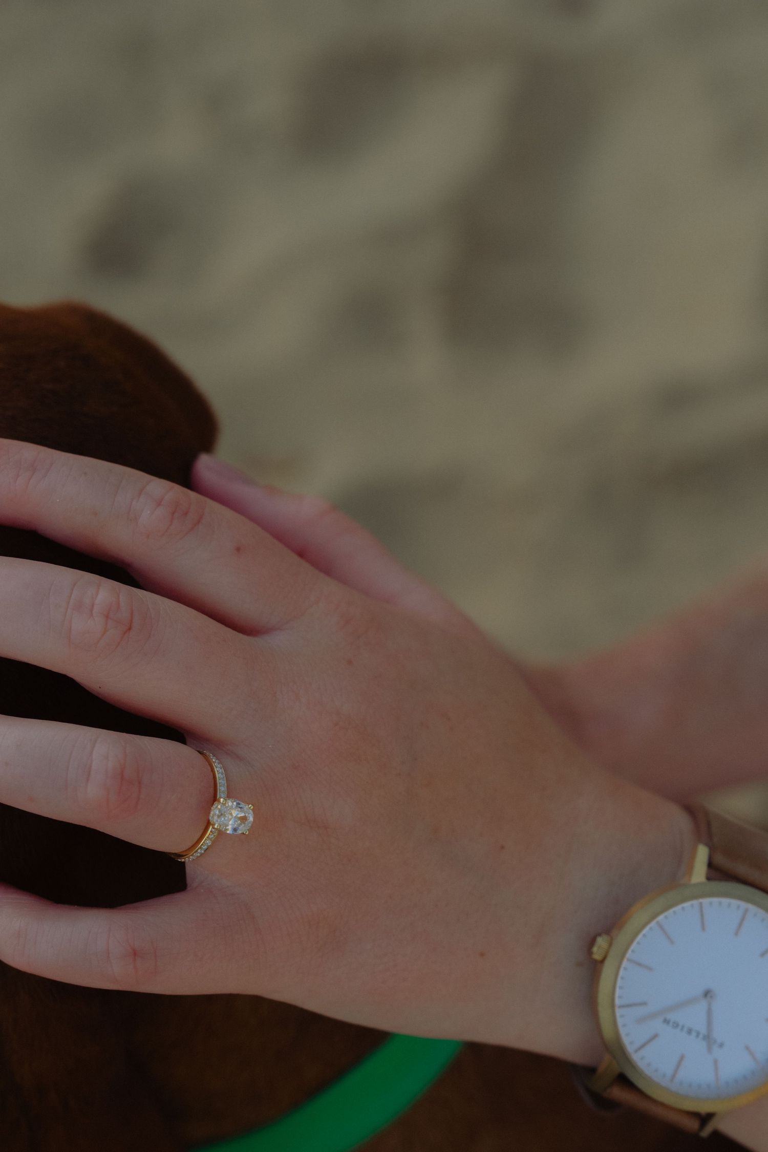 Close-up of an engagement ring on a woman's hand with a gold watch at the beach.